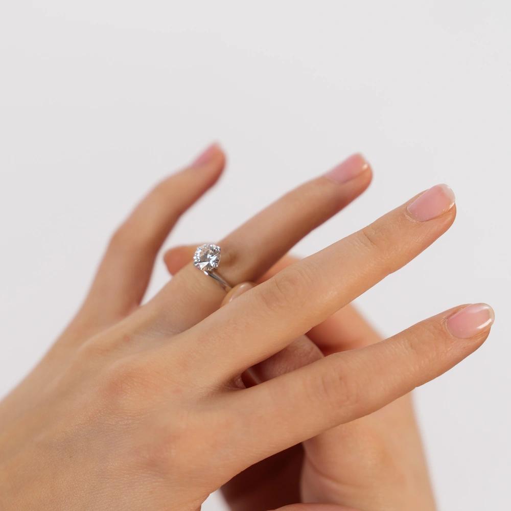 Frau steckt sich einen Verlobungsring aus Weißgold mit einem großem Brillanten an den Ringfinger