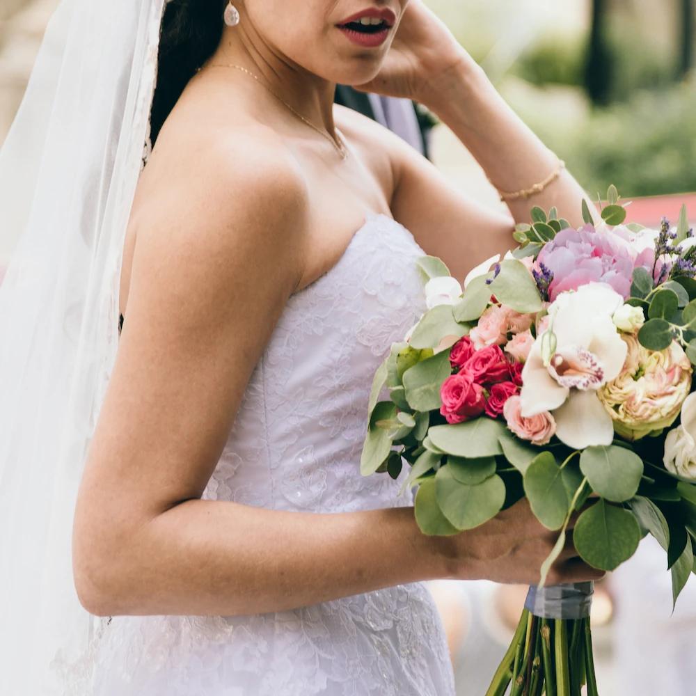 Braut im Hochzeitskleid hält Ihren Brautstrauß in der Hand