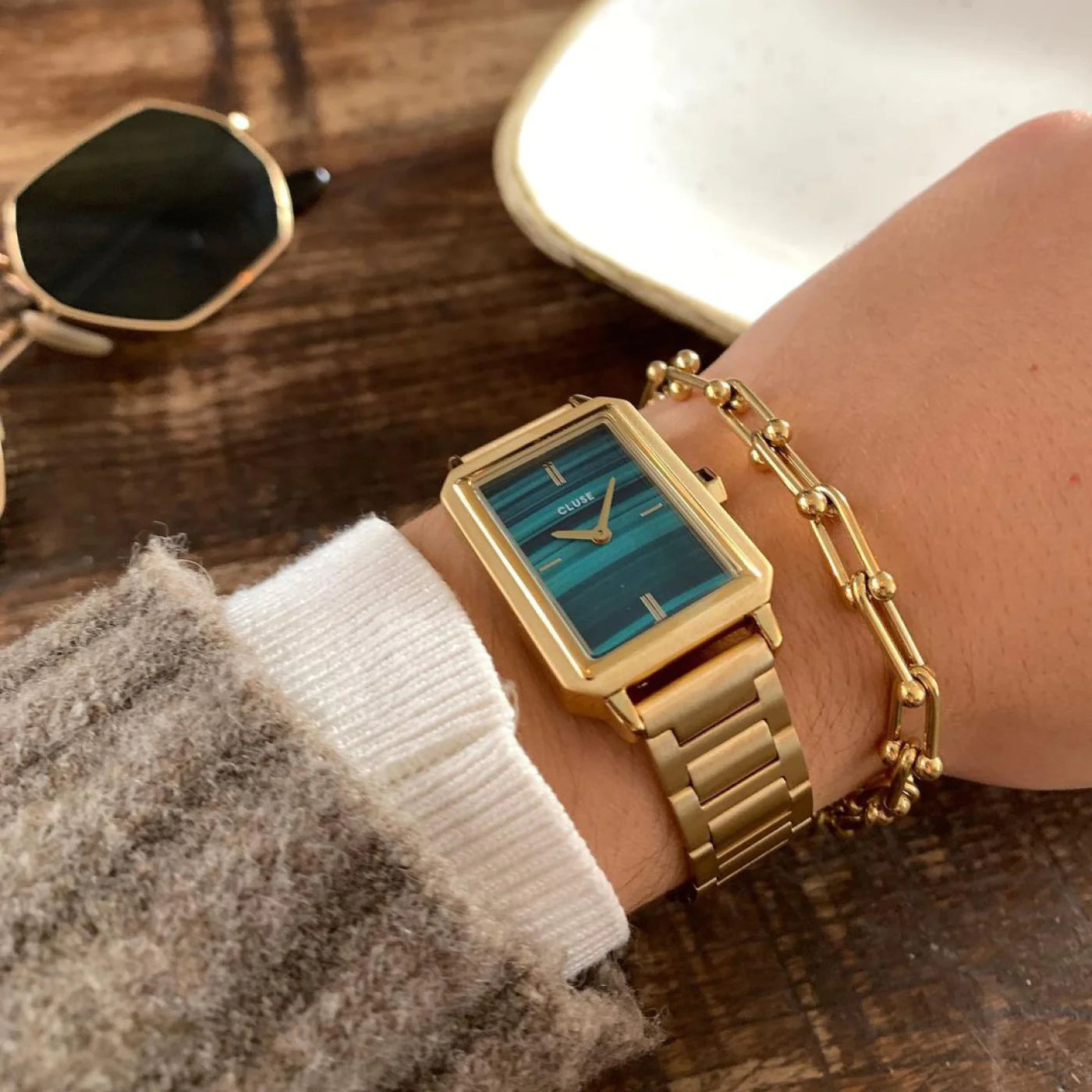 Frau trägt die Cluse "Fluette" Stahl-Uhr mit grünem Malachit-Druck-Zifferblatt mit goldfarbenem Gehäuse und kombiniert es mit einem goldenen Armband