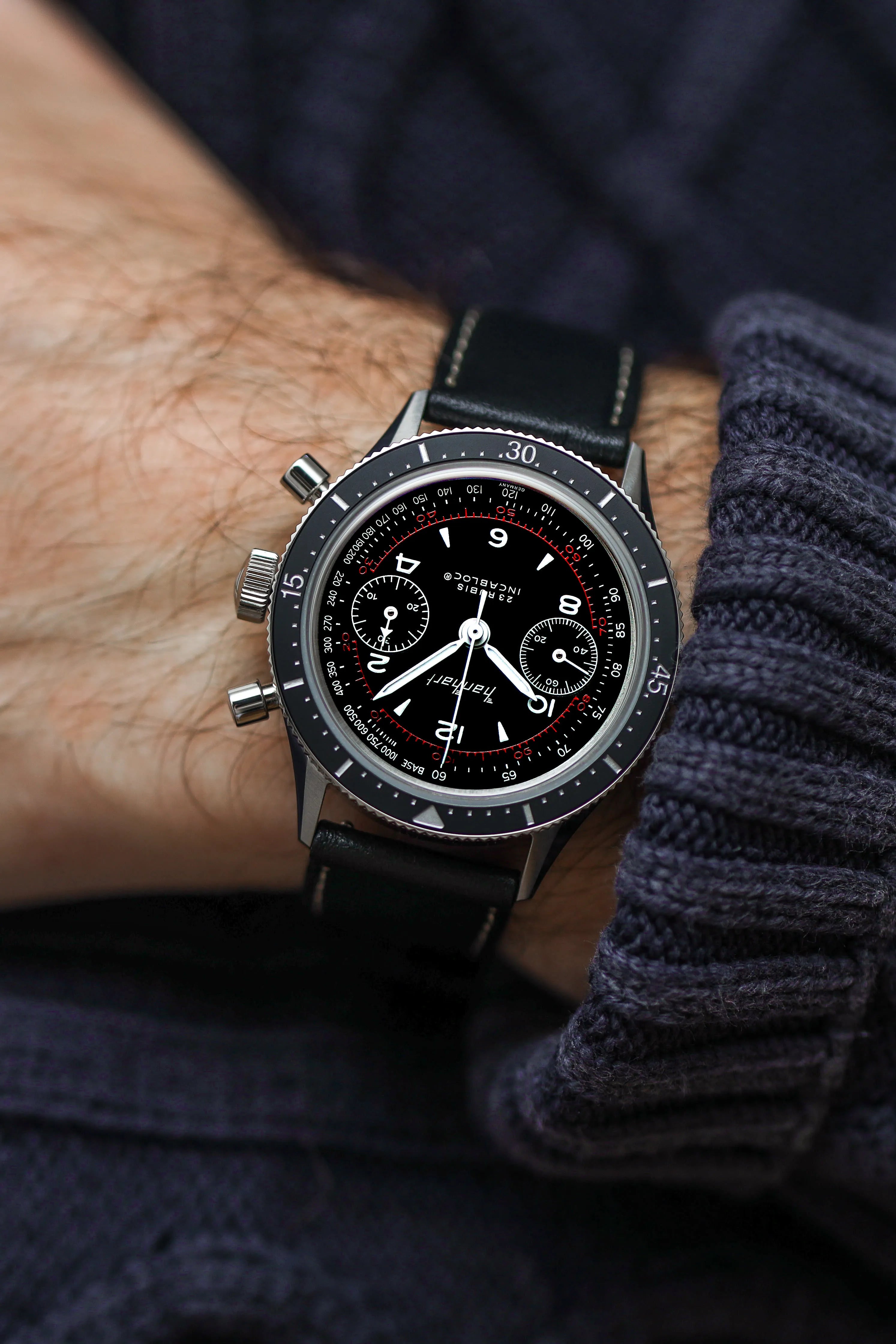 Mann trägt den Hanhart 415 ES Pure Chronographen in Edelstahl mit weißen und roten Details am Lederband und präsentiert die Uhr in die Kamera