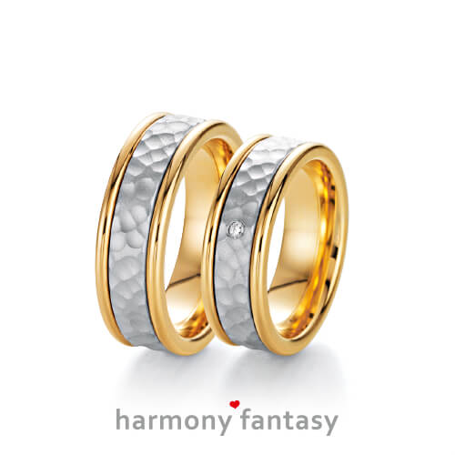Produktfotografie des Trauringpaars Harmony Fantasy in Gelbgold mit eingesetztem Weißgold-Streifen in Hammerschlag-OptikWeißgold, mit einem Diamant im Damenring