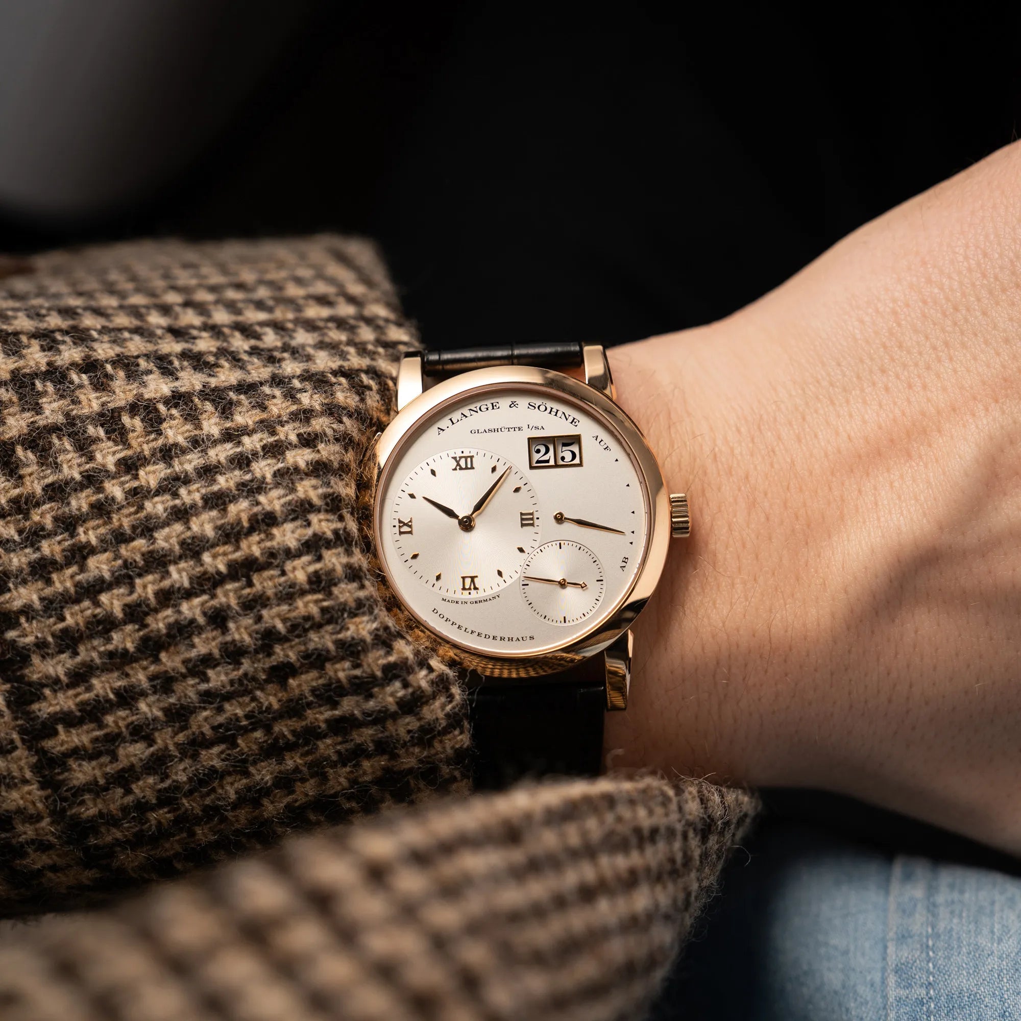Mann in Sakko trägt die A. Lange & Söhne Lange 1 der Referenz 101.032 mit 38,5mm-Roségold-Gehäuse und dem für das Modell typische, asymmetrisch angeordnete Zifferblatt mit Großdatum an seinem Hangelenk