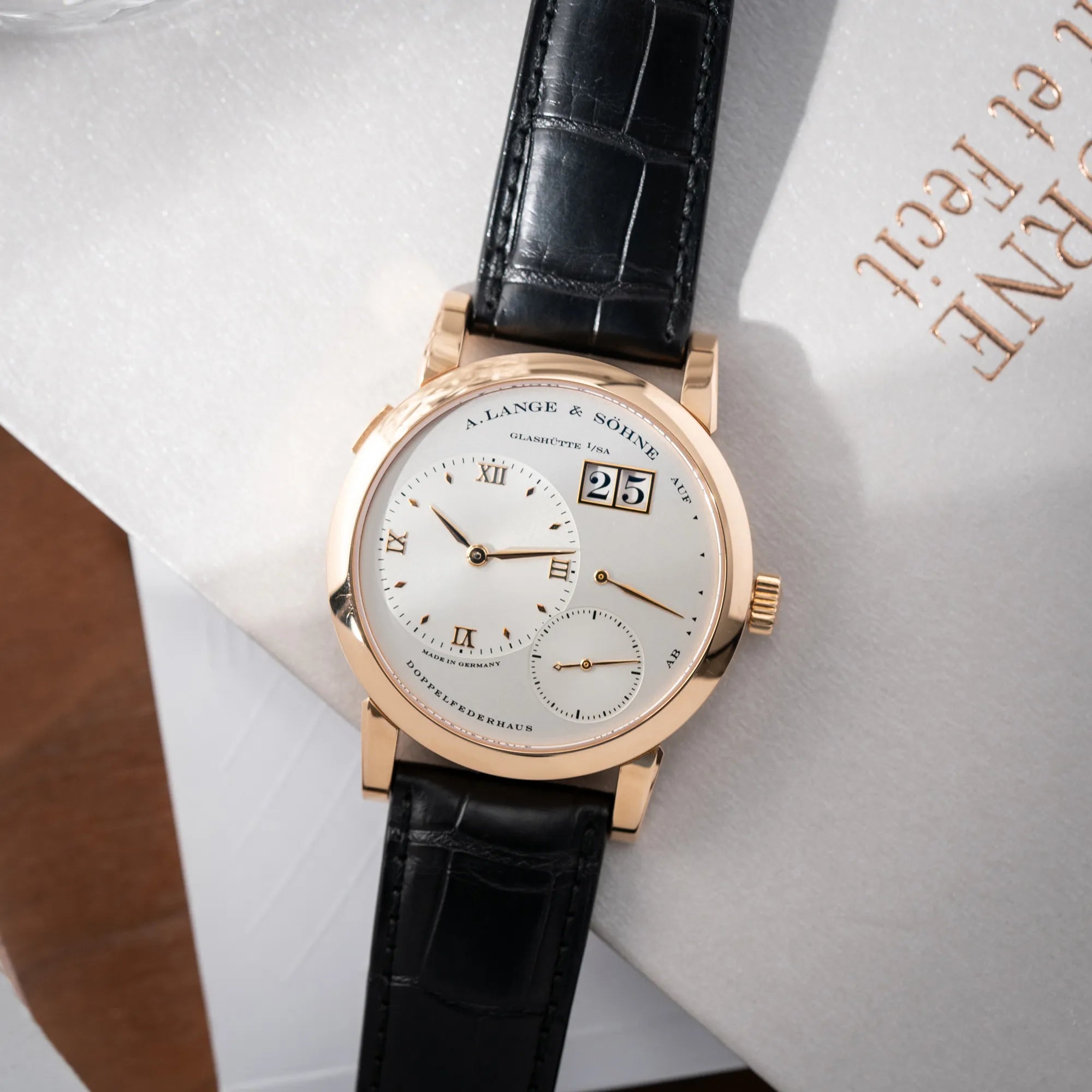 Produktfotografie der flach liegenden A. Lange & Söhne Lange 1 der Referenz 101.032 mit 38,5mm-Roségold-Gehäuse und dem für das Modell typische, asymmetrisch angeordnete Zifferblatt mit Großdatum