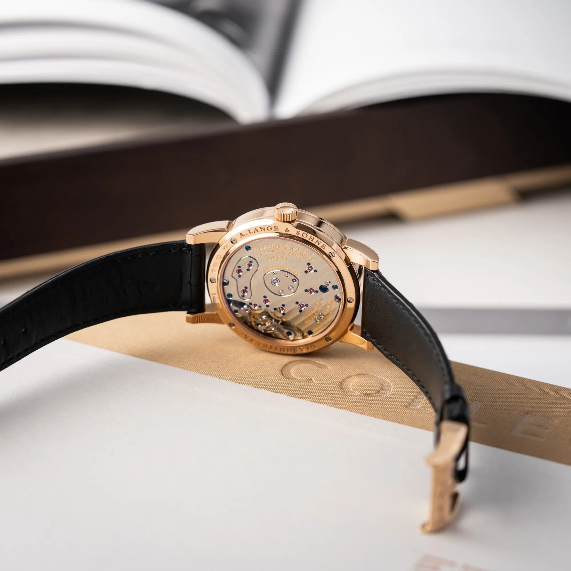 Produktfotografie der A. Lange & Söhne Lange 1 der Referenz 101.032 mit 38,5mm-Roségold-Gehäuse und dem für das Modell typische, asymmetrisch angeordnete Zifferblatt mit Großdatum zeigt die geöffnete Dornschliesse und das Caliber L901.0 durch den Glasboden