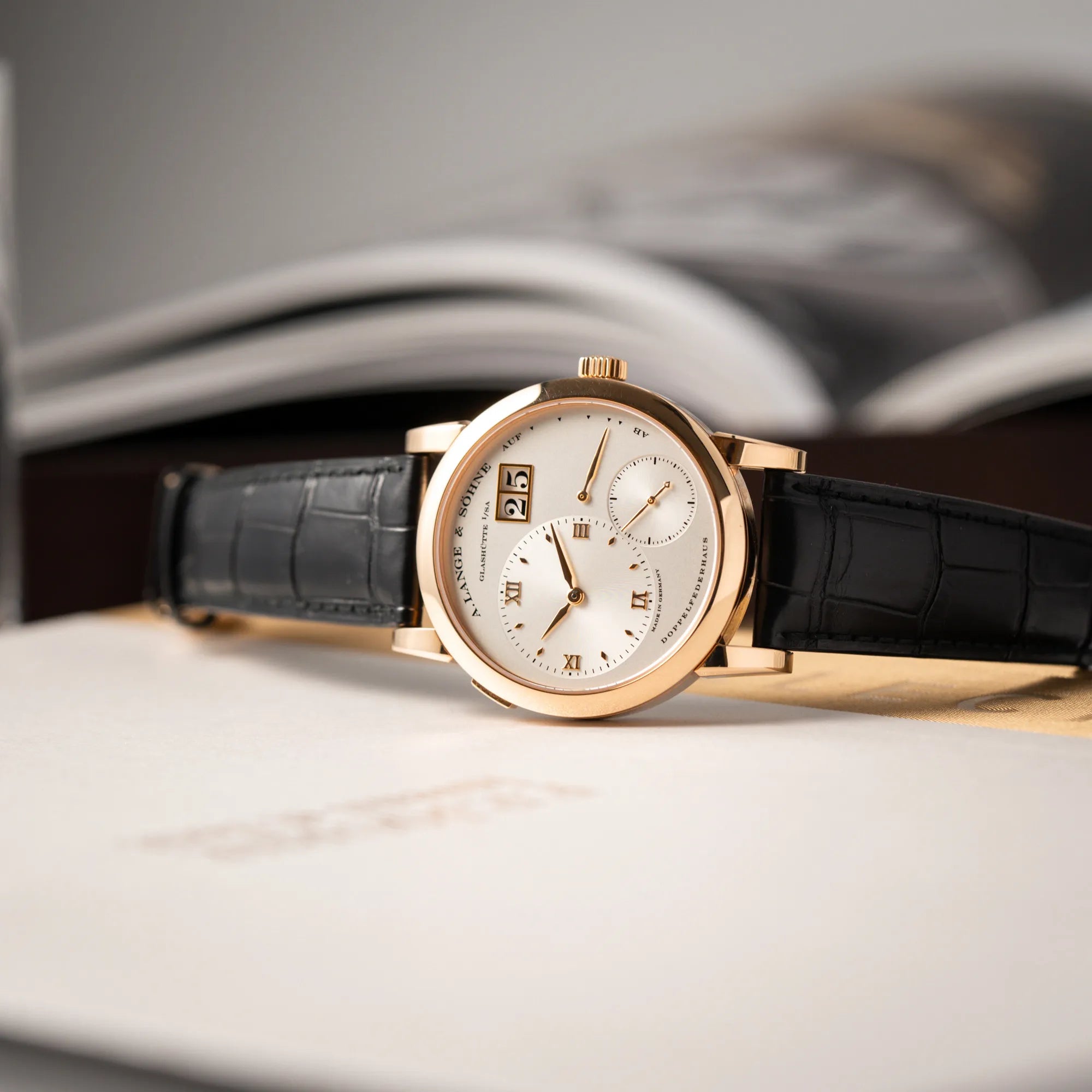 Produktfoto der seitlich auf dem Uhrengehäuse liegenden A. Lange & Söhne Lange 1 der Referenz 101.032 mit 38,5mm-Roségold-Gehäuse und dem für das Modell typische, asymmetrisch angeordnete Zifferblatt mit Großdatum