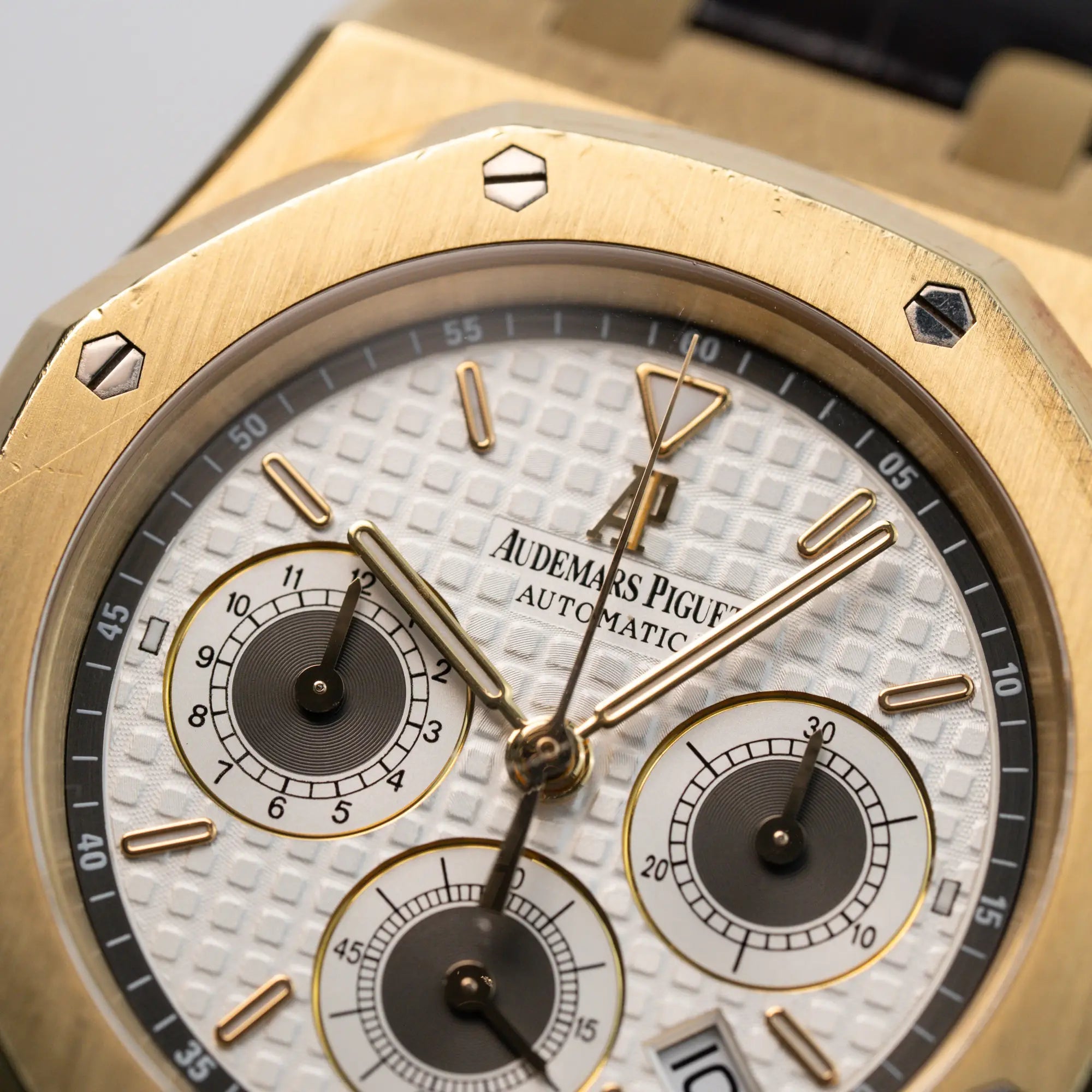 Detailaufnahme des Audemars Piguet Royal Oak Chronograph in Gelbgold mit einem weißen Tapisserie-Zifferblatt am braunen Lederband