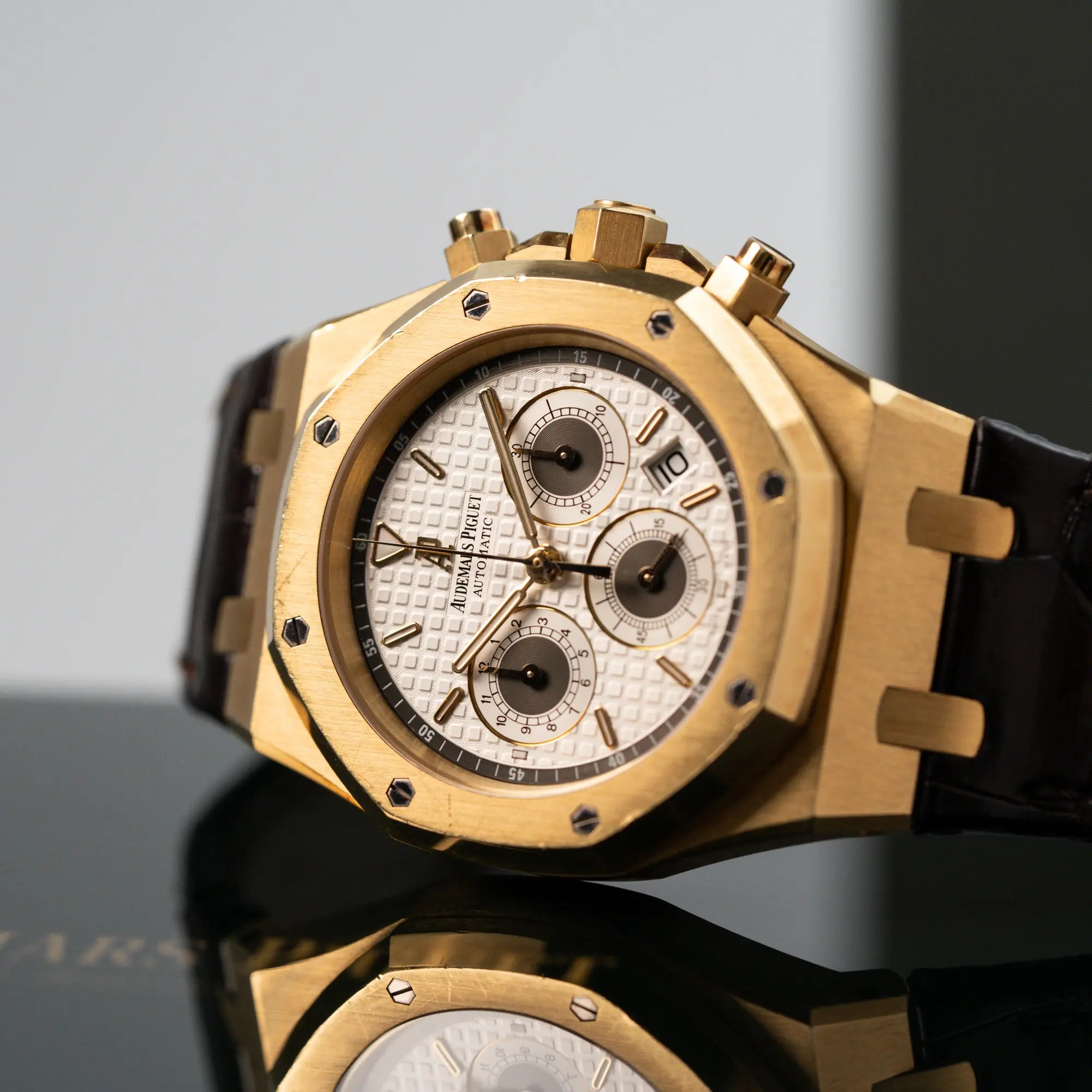 Detailaufnahme des seitlich liegenden gelbgoldenen Royal Oak Chronographs von Audemars Piguet mit einem 39mm Gelbgold-Gehäuse und braunen Lederband
