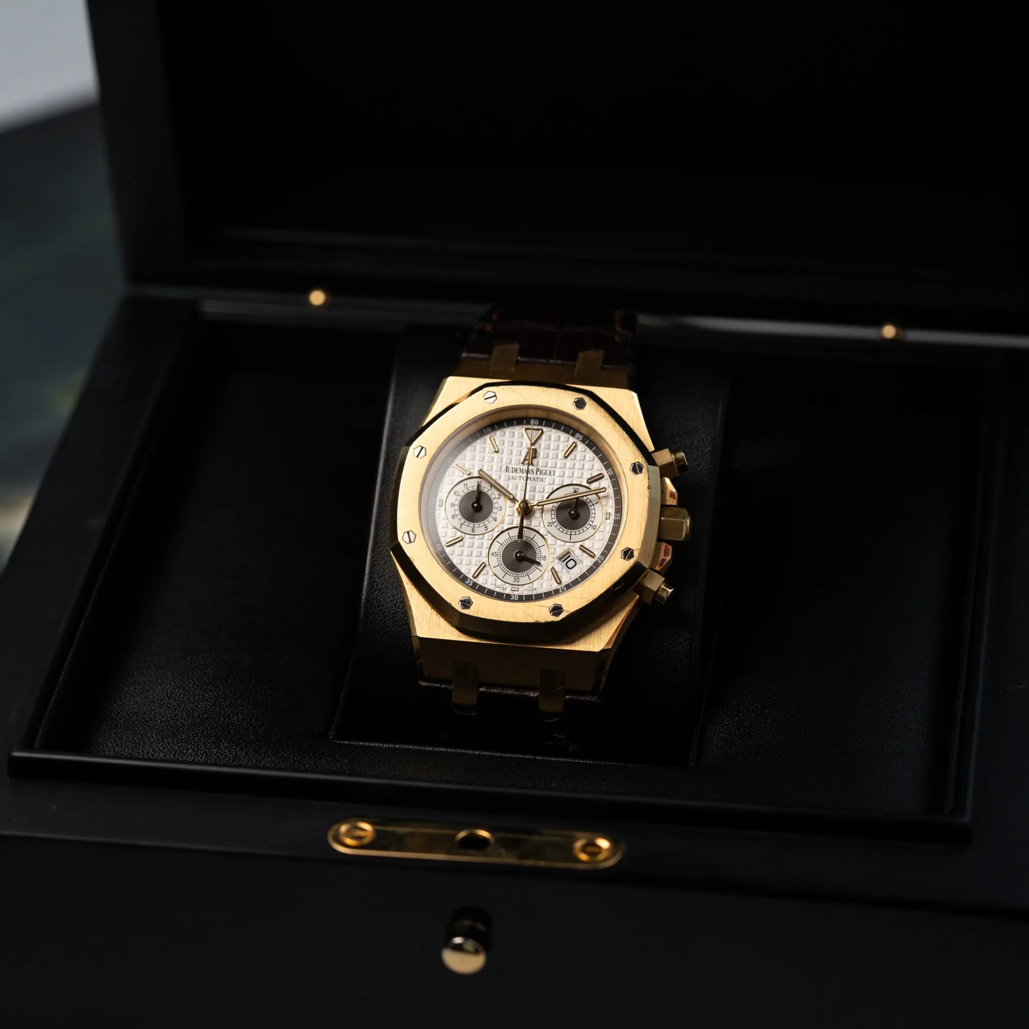 Produktfotografie des gelbgoldenen Royal Oak Chronographs von Audemars Piguet mit einem 39mm Gelbgold-Gehäuse und braunen Lederband, während die Uhr in der Box liegt