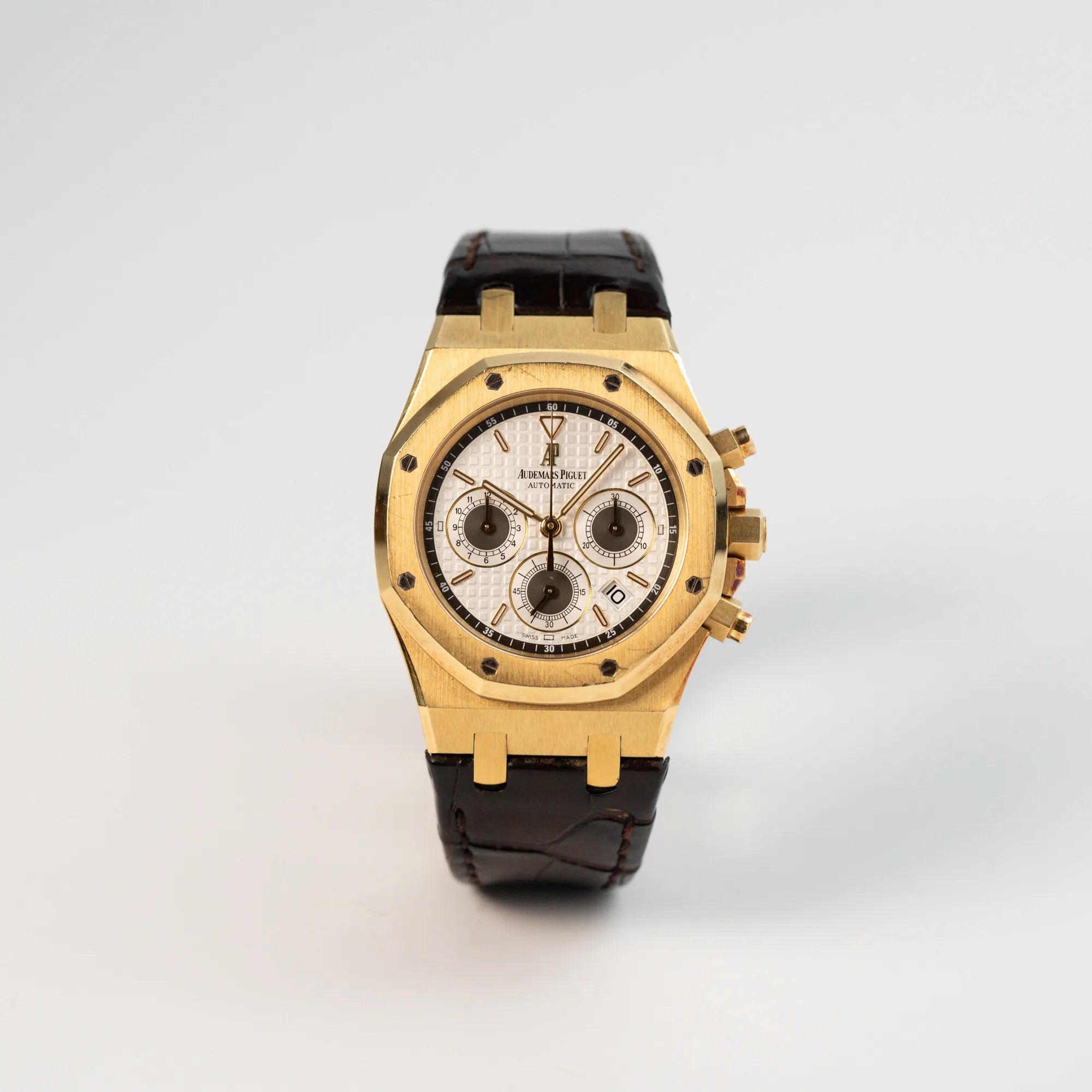 Frontale Ansicht der Audemars Piguet Royal Oak Chronograph in Gelbgold mit einem weißen Tapisserie-Zifferblatt am braunen Lederband