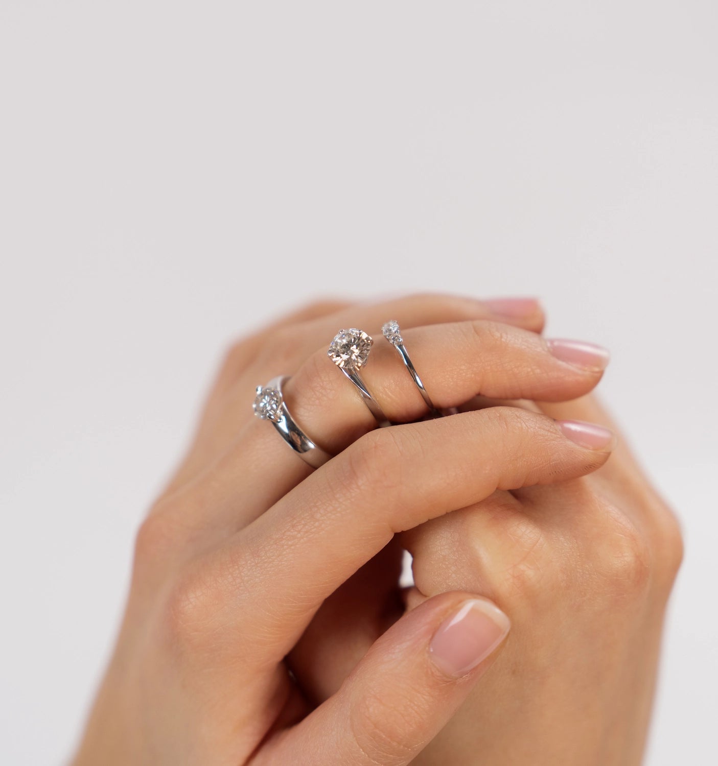 Hand einer Frau präsentiert drei Verlobungsringe auf ihrem Mittelfinger mit verschieden großen Diamanten