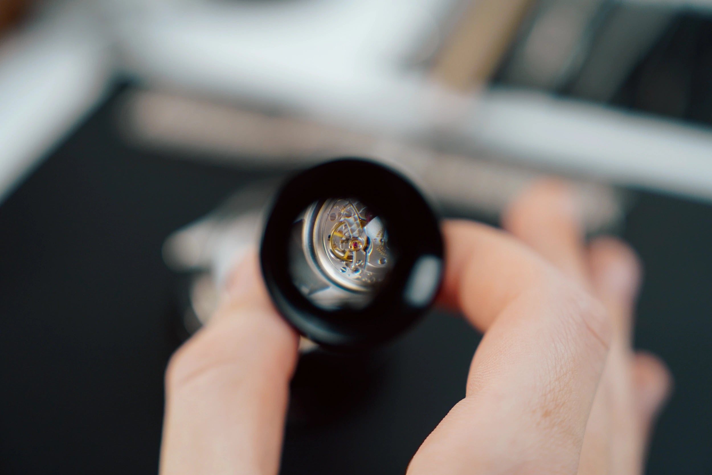 Blick auf ein mechanisches Uhrwerk durch eine Lupe, um die Lupe herum ist alles verschwommen