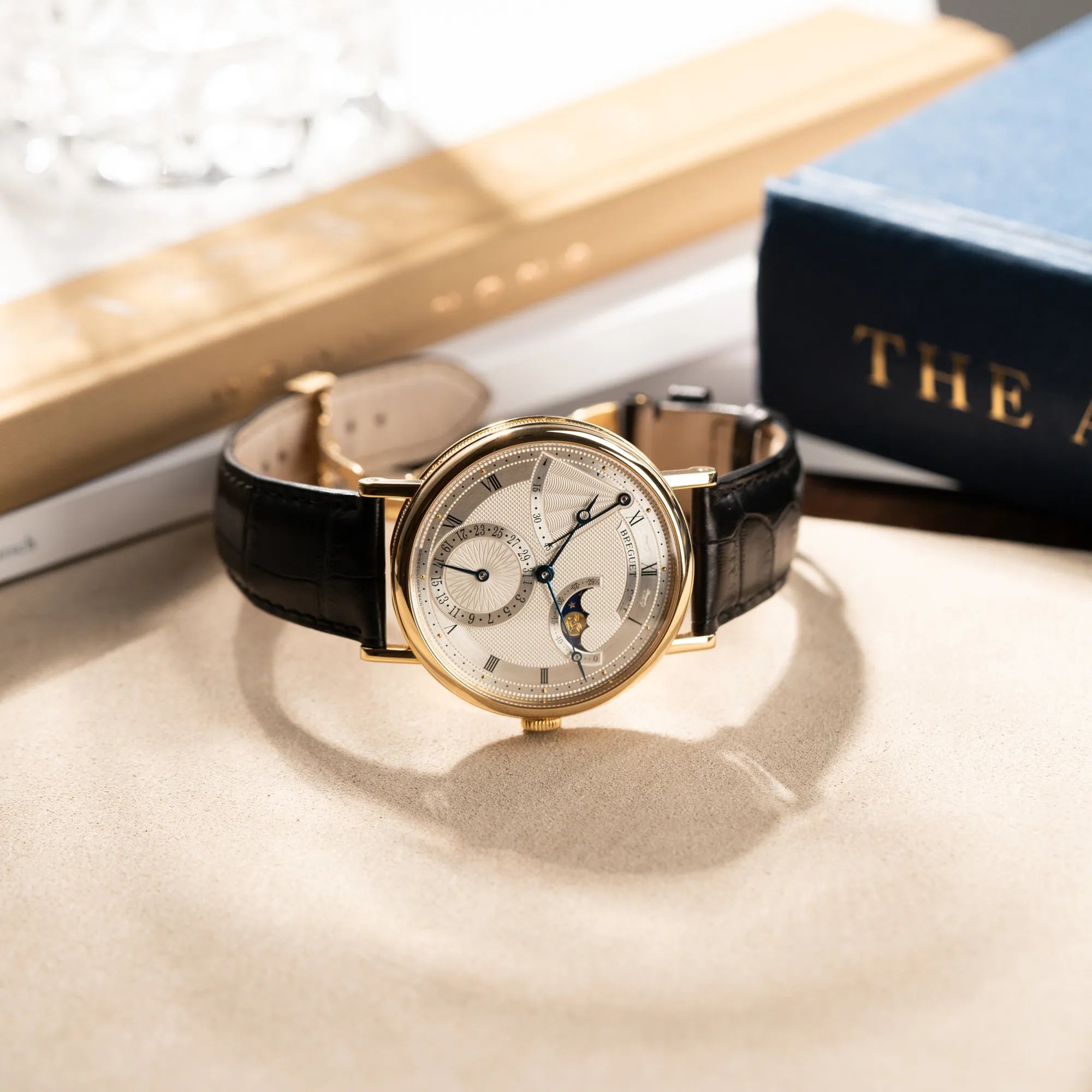 Produktfotografie der seitlich auf dem Gehäuse liegenden Breguet Classique 7137BA mit einem Gelbgoldgehäuse in klassischer Form mit einem silbernen Zifferblatt mit jeweils einem anderen handgefertigten Guilloche-Muster für jede Komplikation