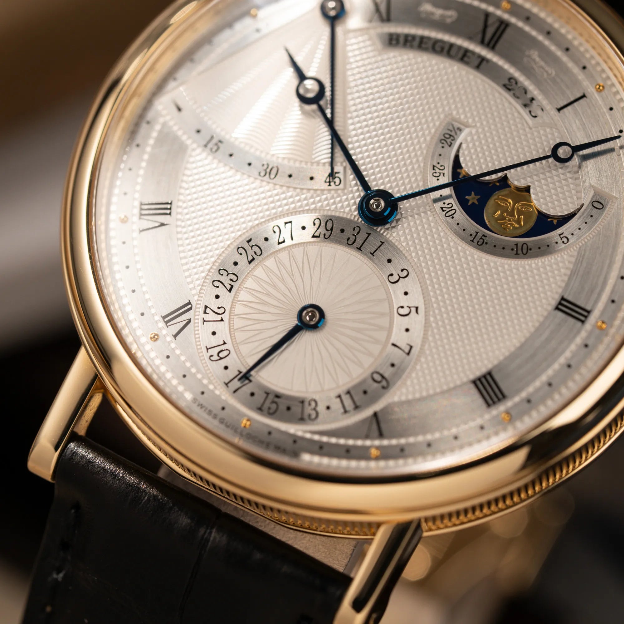 Detailaufnahme der Breguet Classique 7137BA mit einem Gelbgoldgehäuse in klassischer Form mit einem silbernen Zifferblatt mit jeweils einem anderen handgefertigten Guilloche-Muster für jede Komplikation zeigt das Sonnen-Guilloche bei der Datums-Anzeige