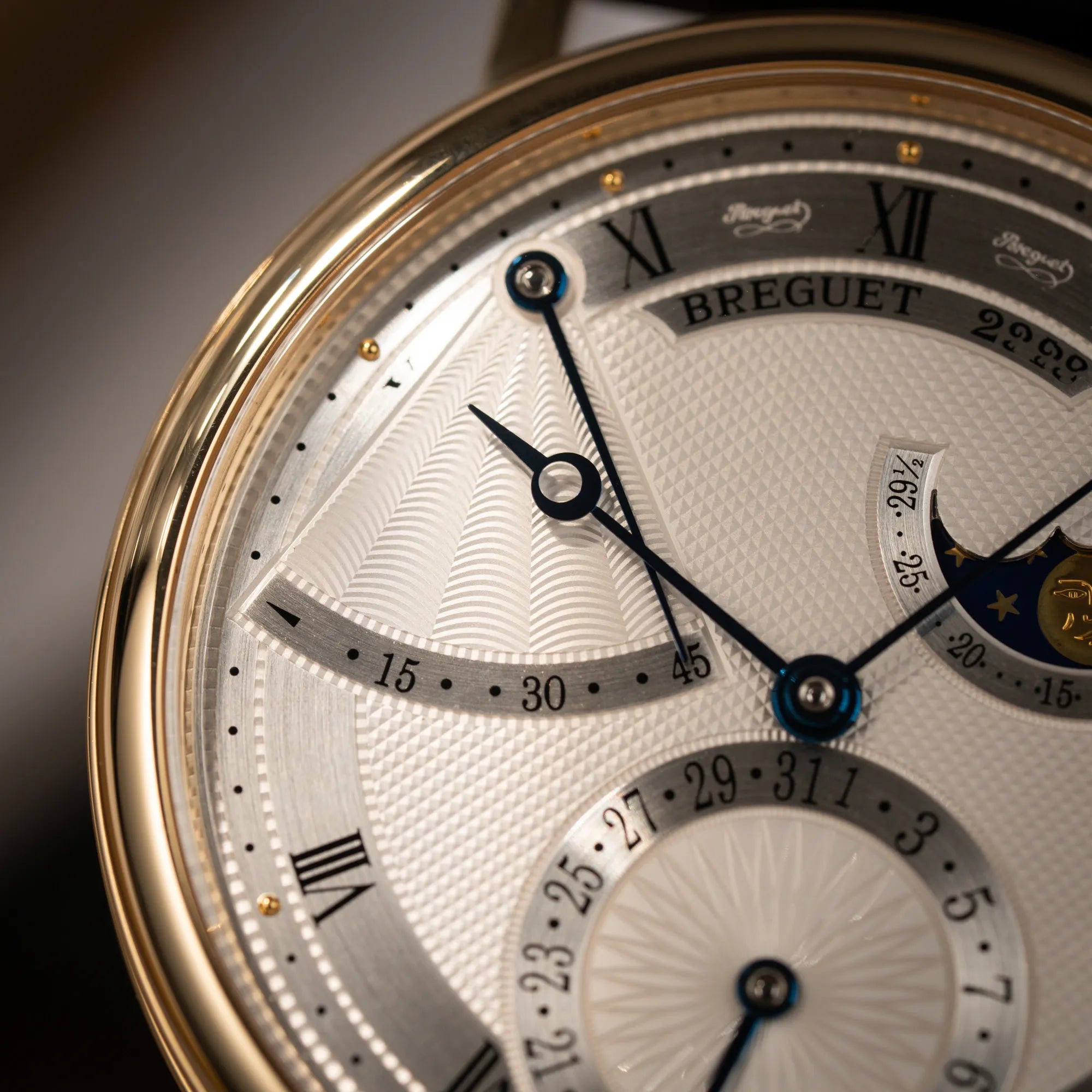Detailaufnahme der Breguet Classique 7137BA mit einem Gelbgoldgehäuse in klassischer Form mit einem silbernen Zifferblatt mit jeweils einem anderen handgefertigten Guilloche-Muster für jede Komplikation zeigt das wellenförmige Guilloche bei der Power-Reserve-Anzeige