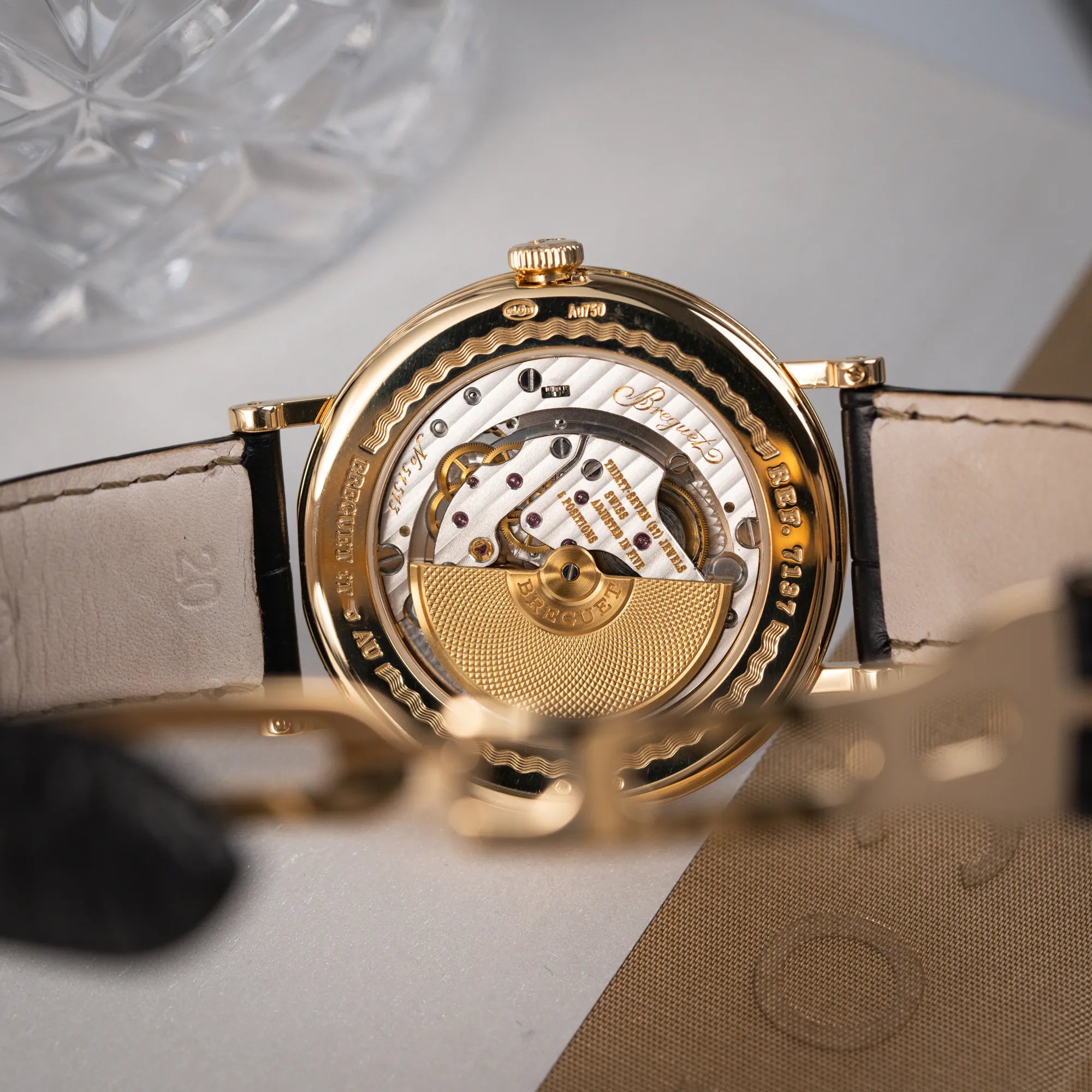 Produktfotografie zeigt das Uhrwerk der Breguet Classique 7137BA mit einem Gelbgoldgehäuse in klassischer Form mit einem silbernen Zifferblatt mit jeweils einem anderen handgefertigten Guilloche-Muster für jede Komplikation durch den gläsernen Gehäuseboden
