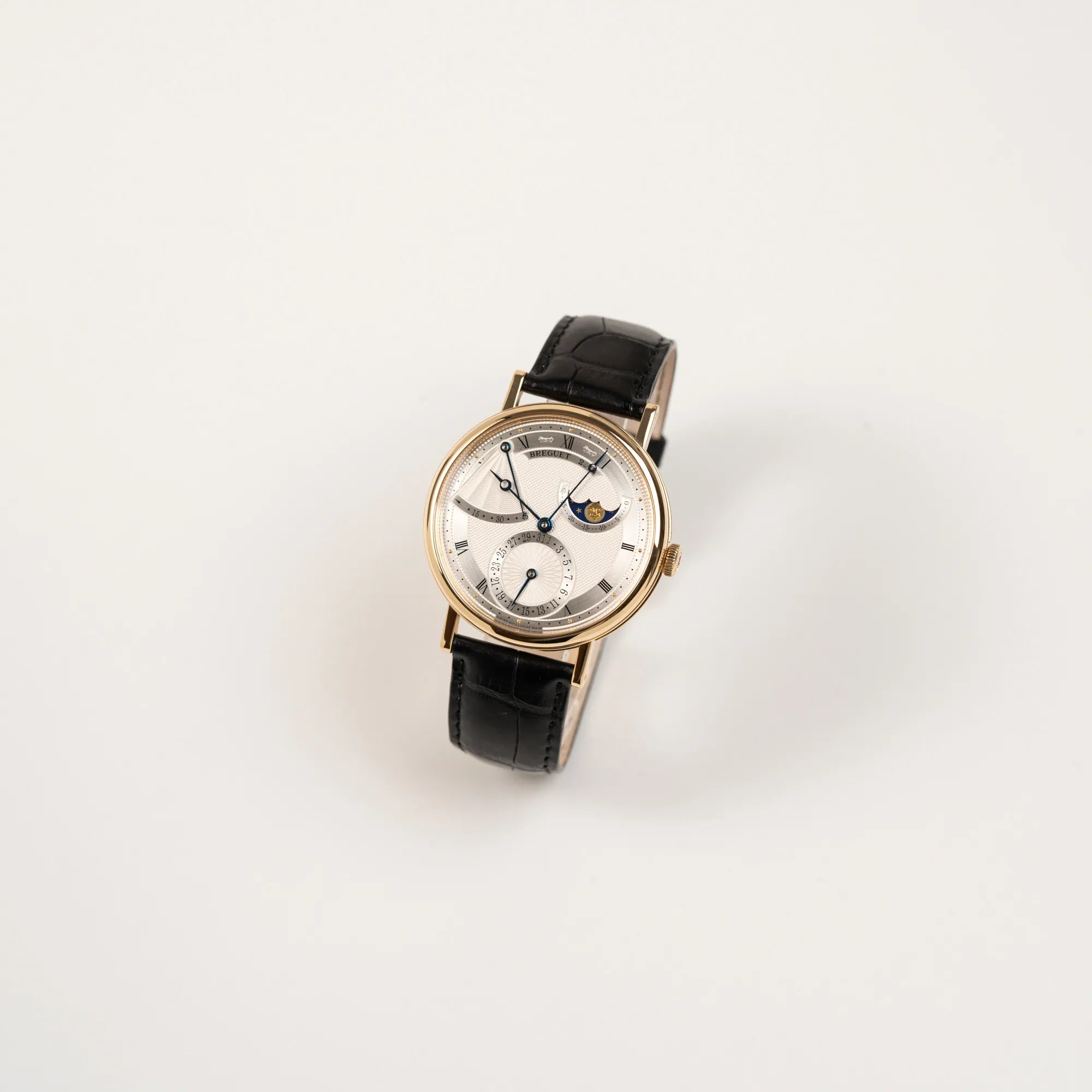 Leicht schräge Ansicht der Breguet Classique 7137BA mit einem Gelbgoldgehäuse in klassischer Form mit einem silbernen Zifferblatt mit jeweils einem anderen handgefertigten Guilloche-Muster für jede Komplikation