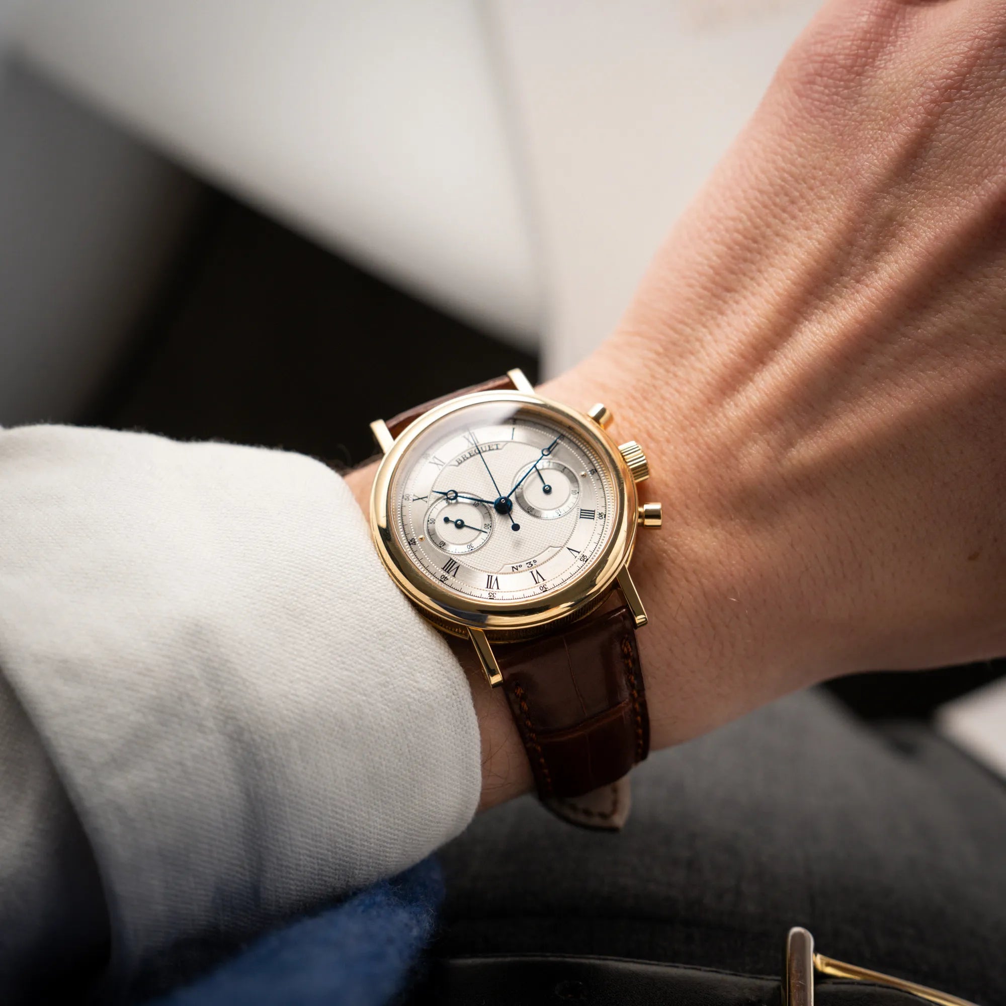 Mann trägt die Breguet Classique Chronograph der Referenz 5237 in Gelbgold mit silbernem guillochiertem Zifferblatt am braunem Lederband an seinem Handgelenk