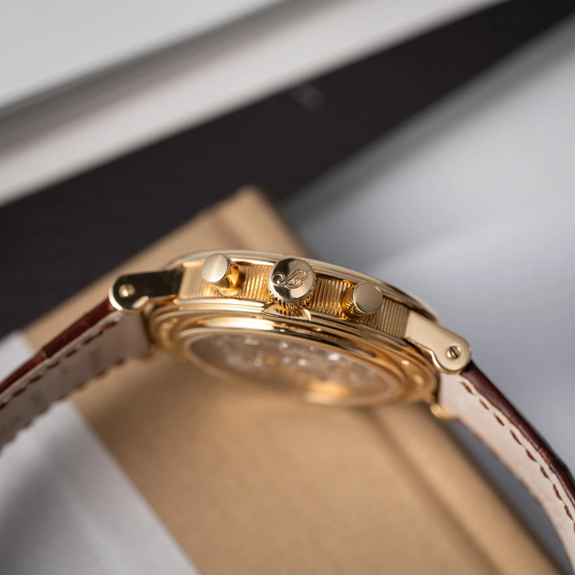 Produktfotografie zeigt die seitliche, kannelierte Gehäusflanke mit Blick auf die Aufzugskrone und Chronograph-Drücker des Breguet Classique Chronograph der Referenz 5237 in Gelbgold mit silbernem guillochiertem Zifferblatt am braunem Lederband