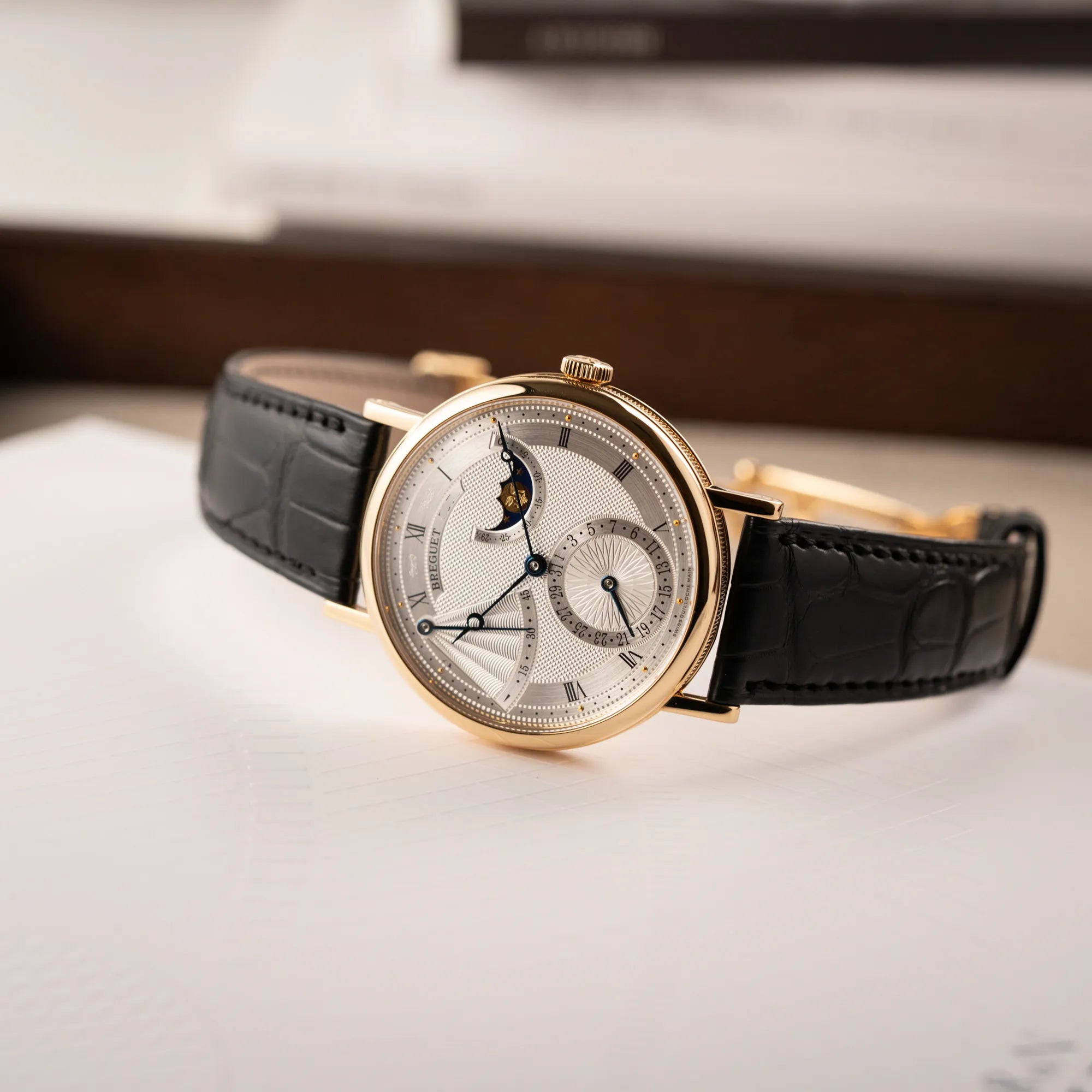 Fotografie der Breguet Classique Mondphase 7137 in Gelbgold mit silbernen, verschieden guillochiertem Zifferblatt zeigt die verschiedenen Spiegelungen auf dem Guilloche-Zifferblatt