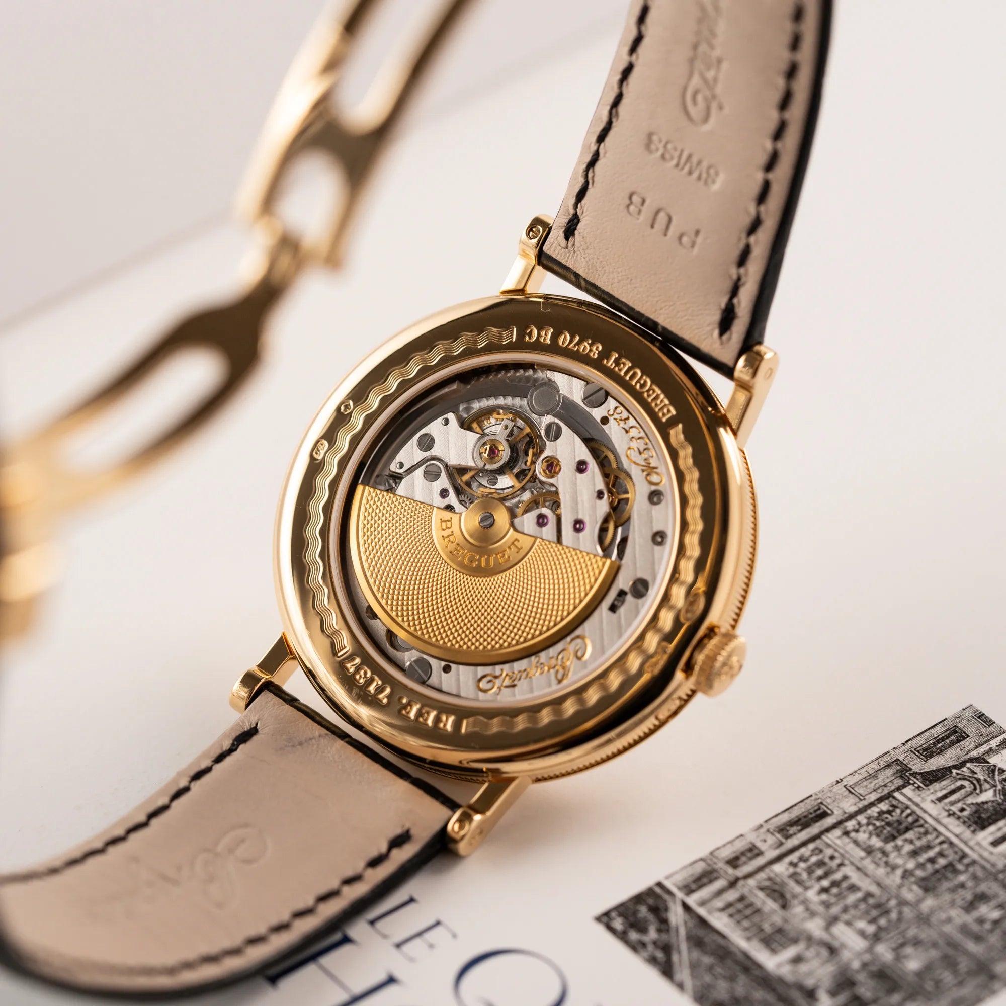 Produktfotografie der Breguet Classique Mondphase 7137 in Gelbgold mit silbernen, verschieden guillochiertem Zifferblatt zeigt den Gehäuseboden aus Glas und das Uhrwerk 502.3 DR1 mit Microrotor