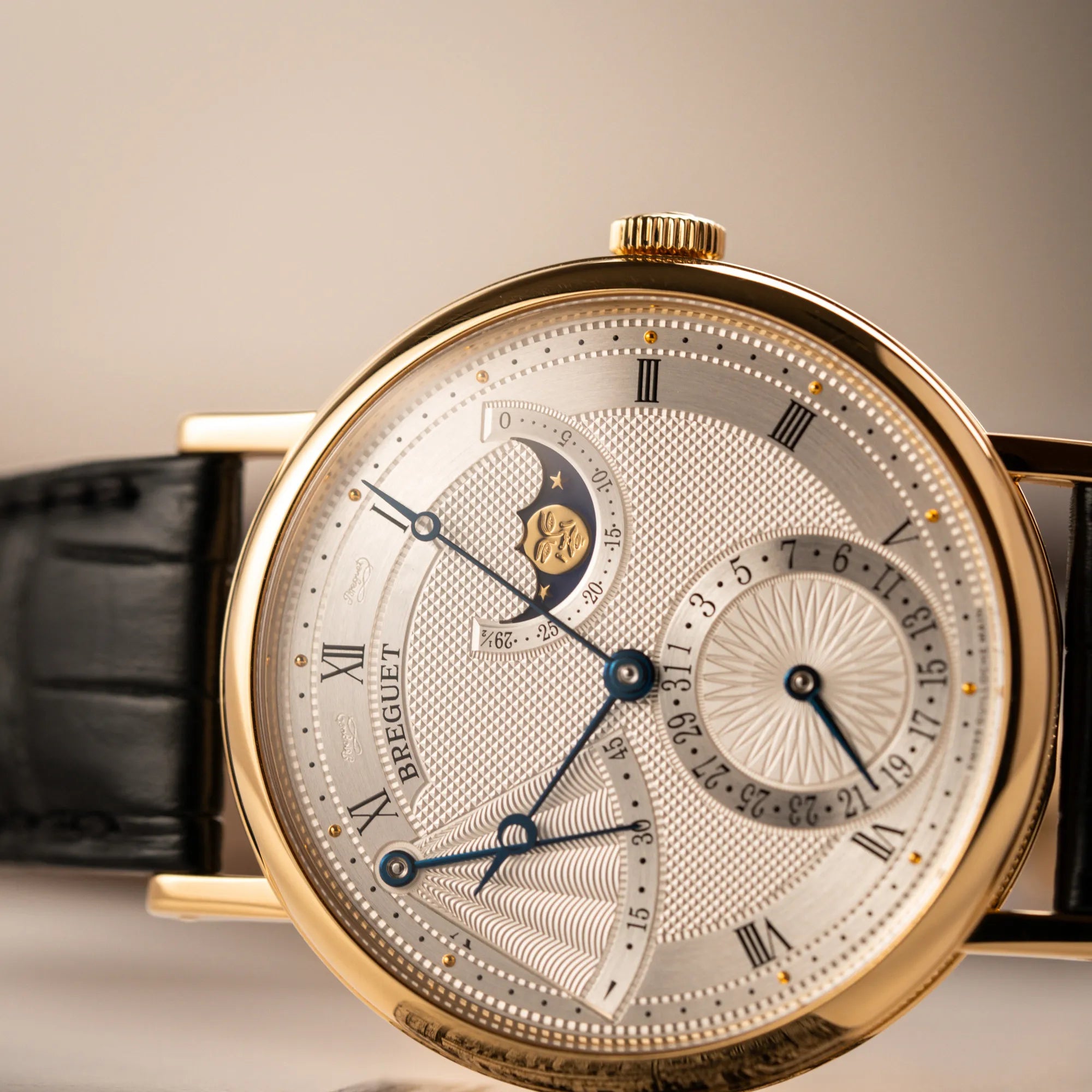 Detailaufnahme der seitlich liegenden Breguet Classique Mondphase 7137 in Gelbgold mit silbernen, verschieden guillochiertem Zifferblatt