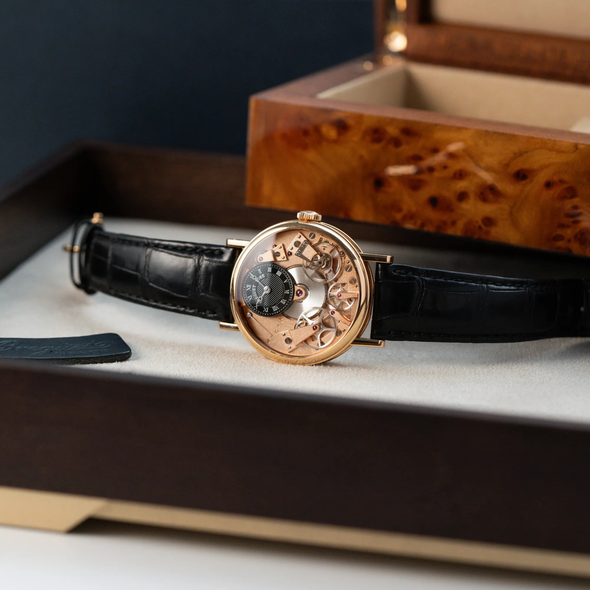 Produktfotografie der klassischen Breguet Tradition Armbanduhr mit Rosegold-Gehäuse und schwarzem Zifferblatt zusammen mit der Uhrenbox aus Wuzelholz