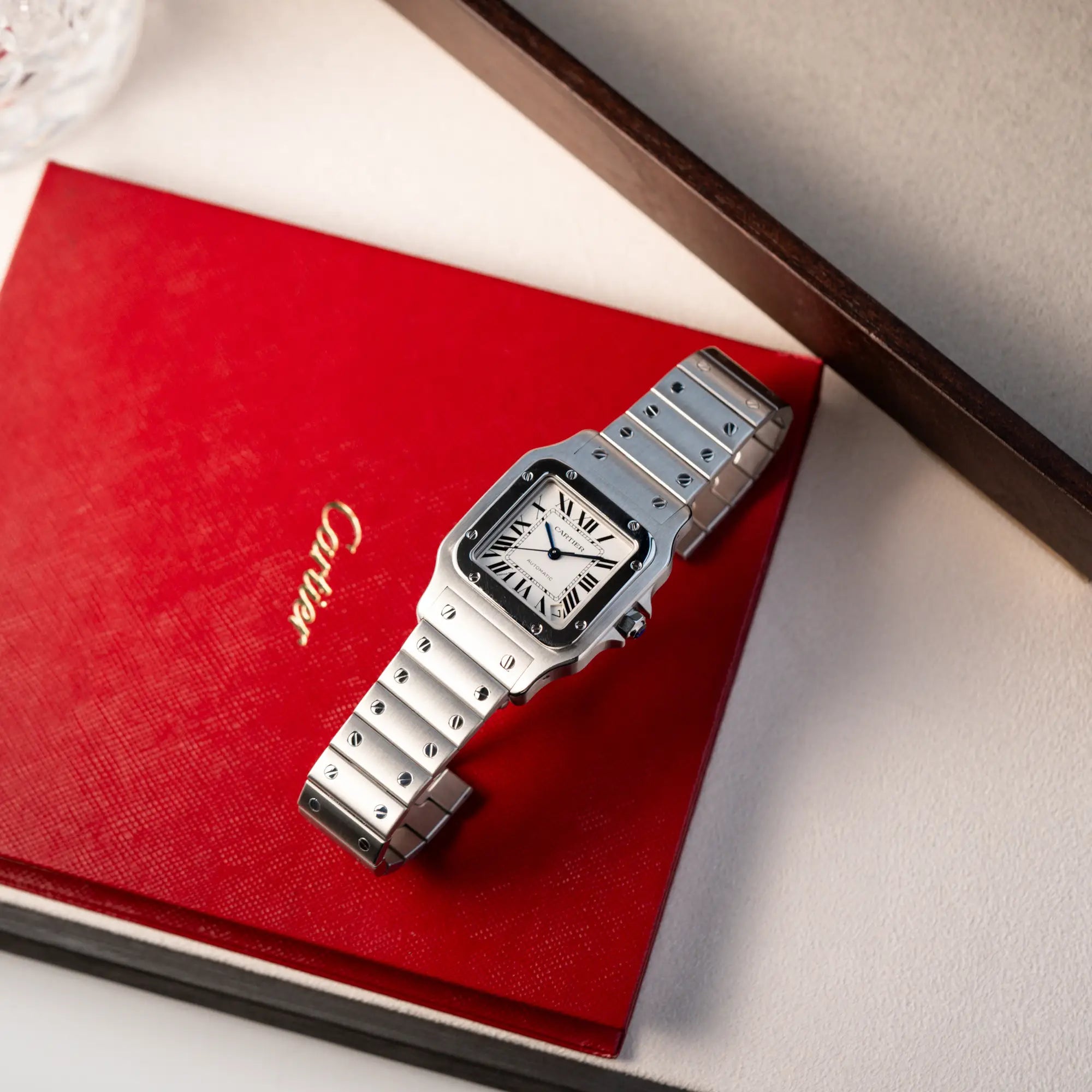 Produktfotografie der Cartier Santos Galbée 2823 in Edelstahl mit weißem Zifferblatt zusammen mit den Papieren in klassischer roter-Cartier Verpackung