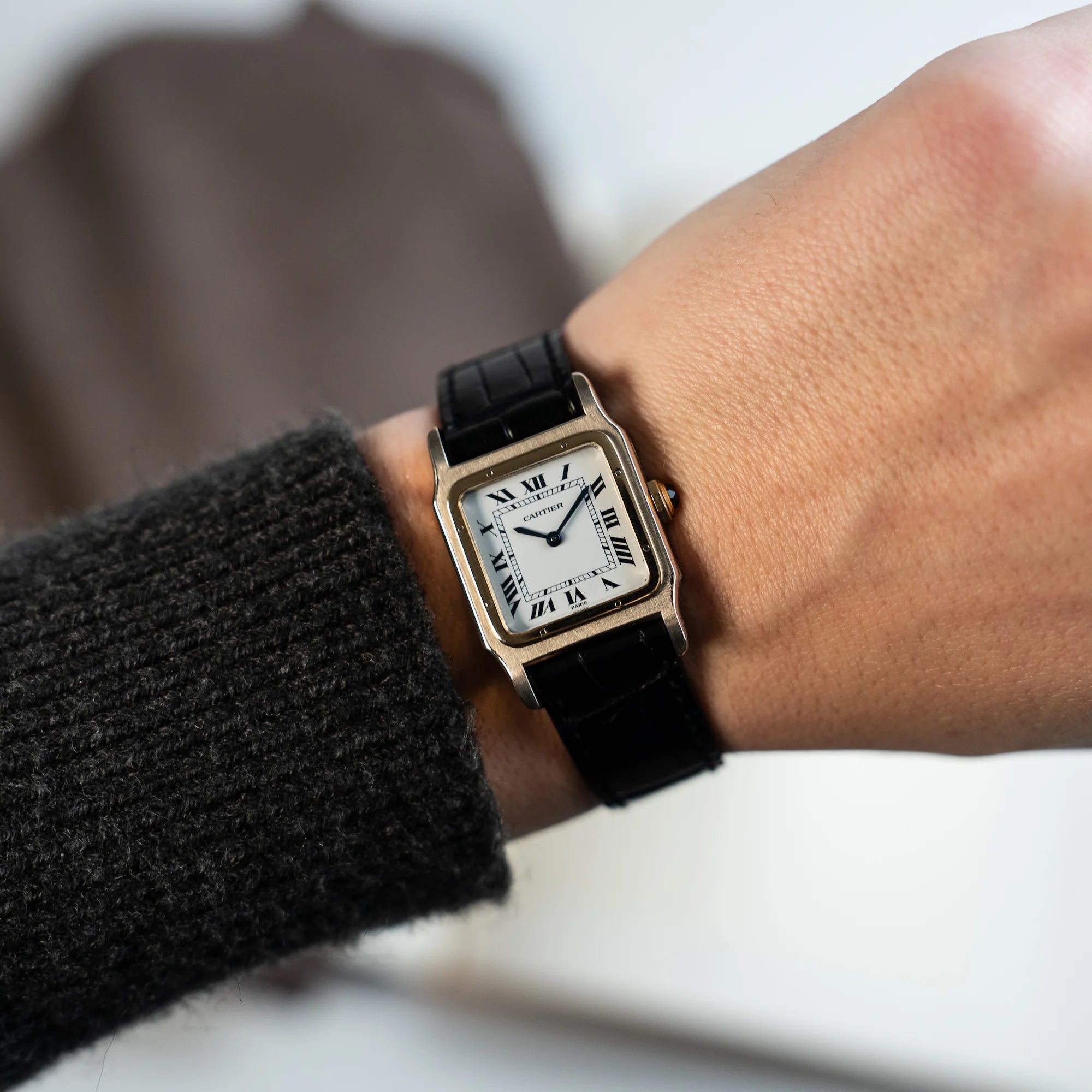 Mann trägt die Cartier Santos Dumont "Deux Ors" mit Paris Dial am schwarzen Lederarmband an seinem Handgelenk