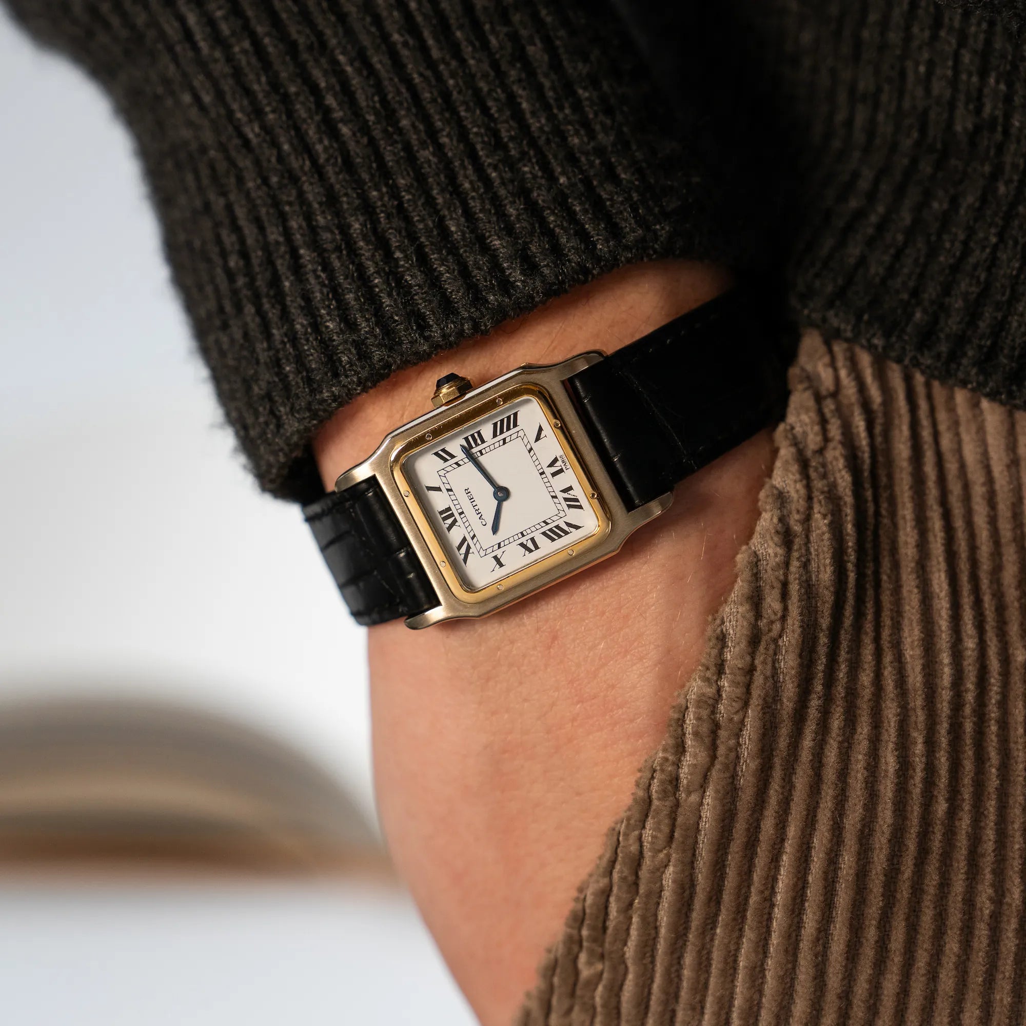 Mann trägt die Cartier Santos Dumont "Deux Ors" mit Paris weißem Paris Dial am Handgelenk, während er seine Hand in seine Hosentasche steckt