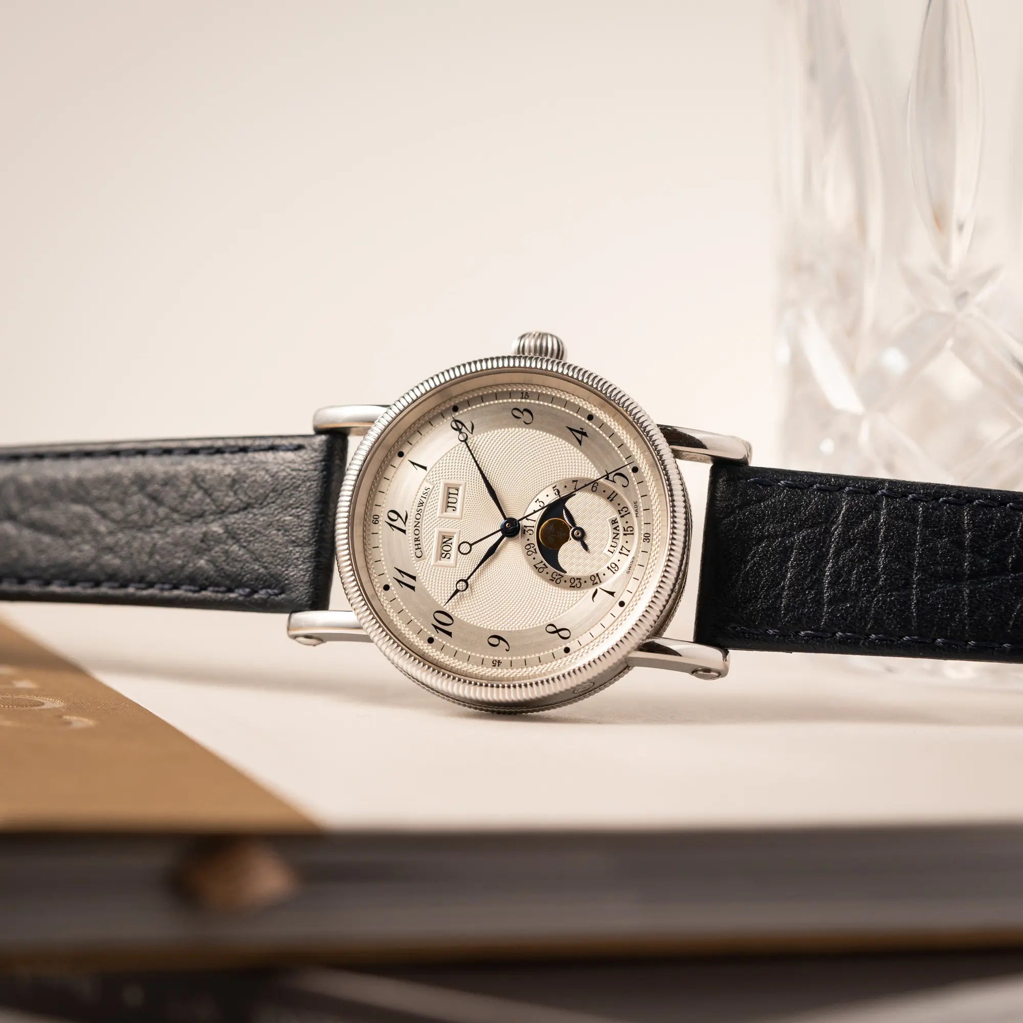 Produktfotografie als Titelbild der Chronoswiss Klassic Luna Mondphase CH9323 mit silbernem, guillochiertem Zifferblatt mit Kalenderanzeige auf 12 Uhr und einer Mondphase-Anzeige bei 6 Uhr