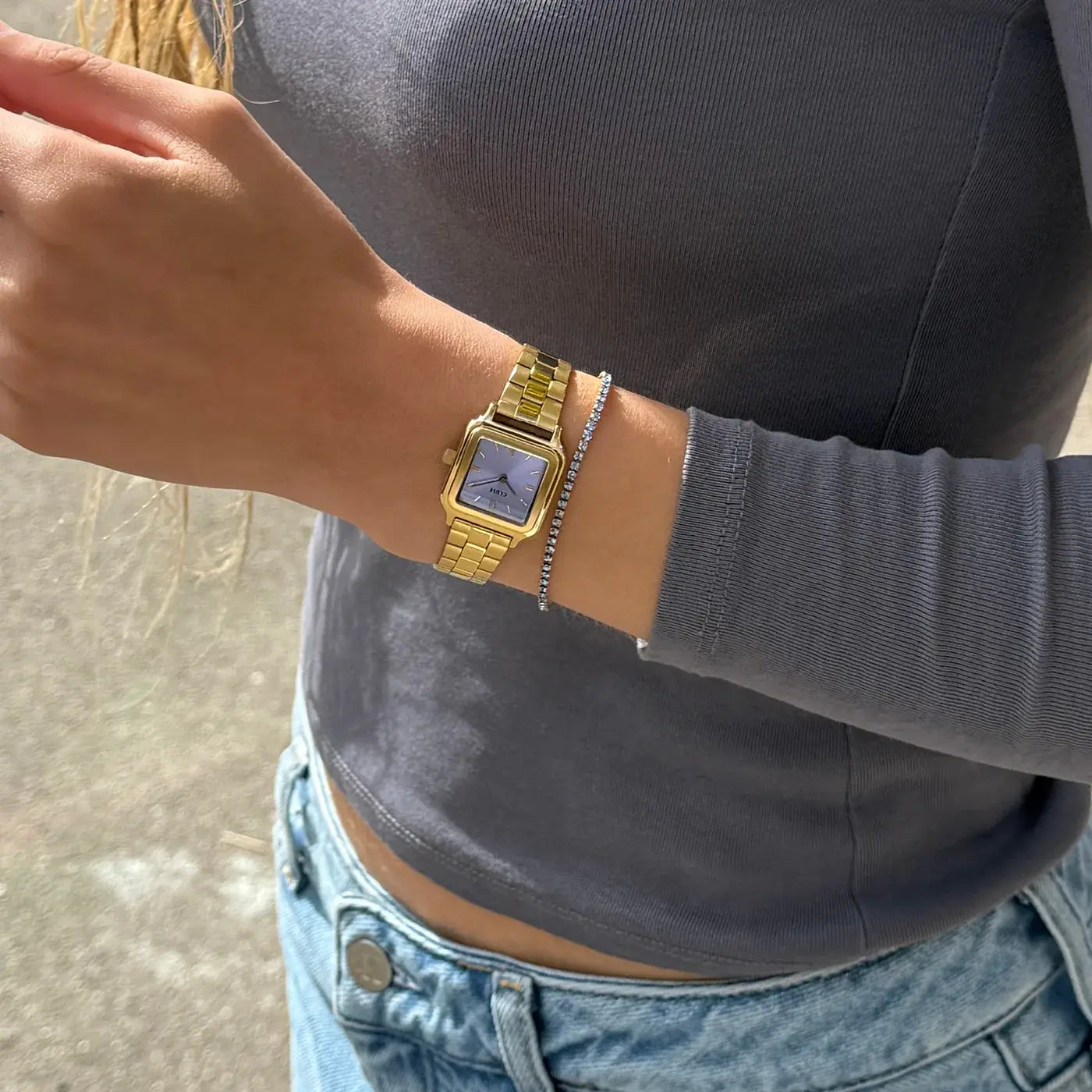 Lifestyleshot einer Frau mit der der goldfarbenen Cluse Gracieuse Petite Damenuhr mit rechteckigem Gehäuse und lila, flieder-farbenem Zifferblatt am Handgelenk