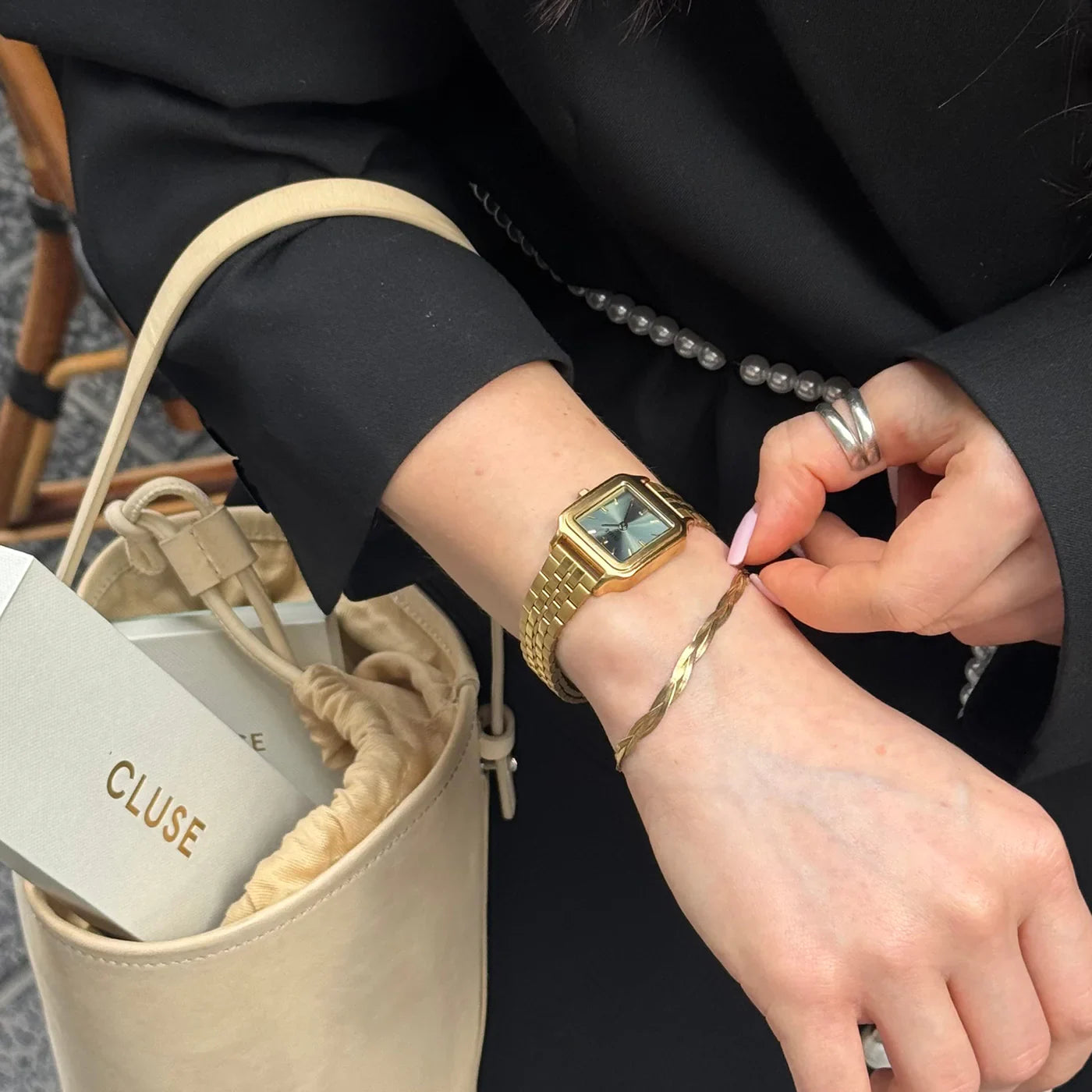Lifestyle-Foto einer Frau mit der goldfarbenen Cluse Gracieuse Petite Damenuhr mit rechteckigem Gehäuse und salbeigrünem Zifferblatt am Handgelenk