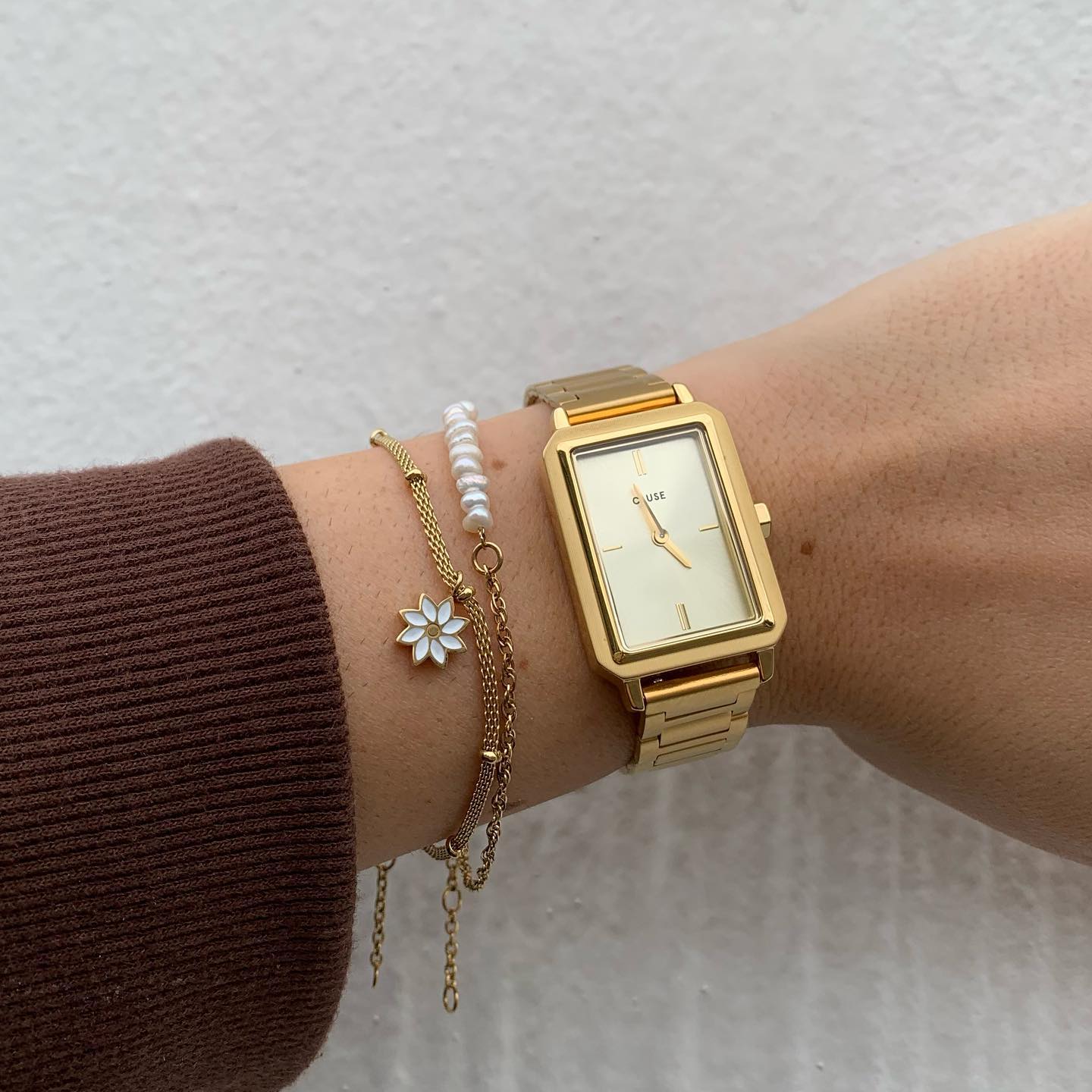 Frau trägt die Cluse "Fluette" Stahl-Uhr mit gelbgold-farbenem Zifferblatt und Gehäuse und kombiniert dieser mit gelbgoldenen Armbändern