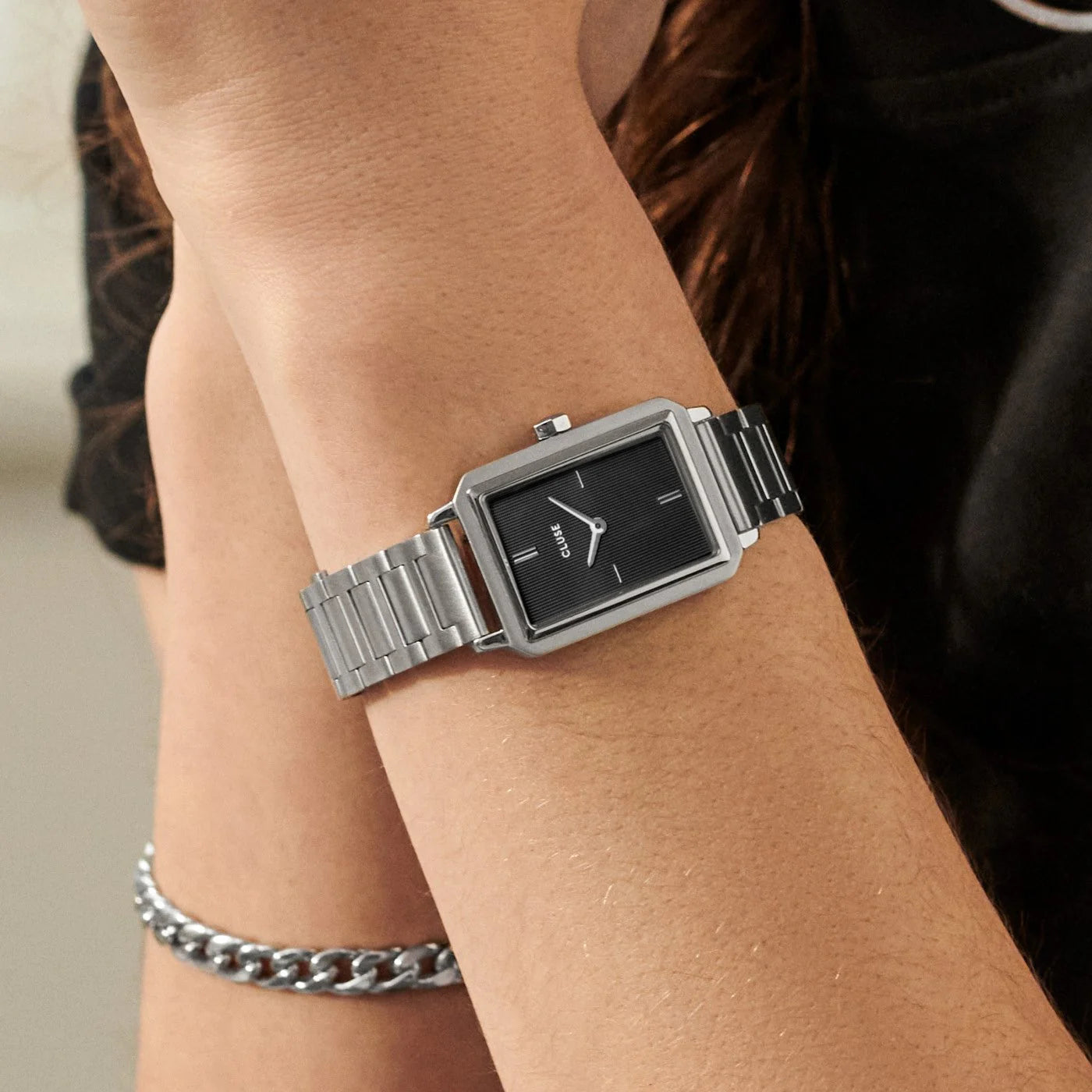 Frau trägt die Cluse "Fluette" Stahl-Uhr mit schwarzem, gestreiften Zifferblatt mit silberfarbenem Gehäuse mit Edelstahl-Armband 