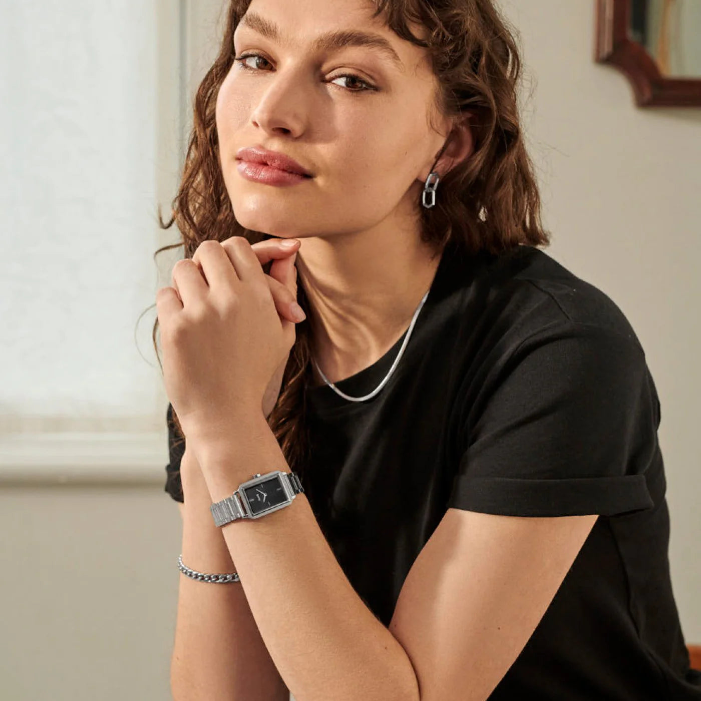 Frau in schwarzem T-Shirt trägt die Cluse "Fluette" Stahl-Uhr mit schwarzem, gestreiften Zifferblatt mit silberfarbenem Gehäuse mit Edelstahl-Armband