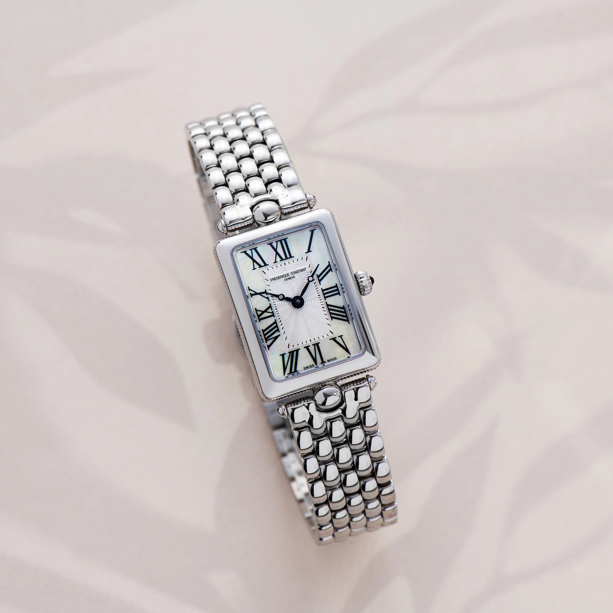 Produktfotografie der Frederique Constant Art Deco Carre aus der Classics Kollektion mit einem rechteckigen Uhrengehäuse mit einem Zifferblatt in Perlmutt-Optik und schwarzen, römischen Ziffern auf einem beigen Hintergrund