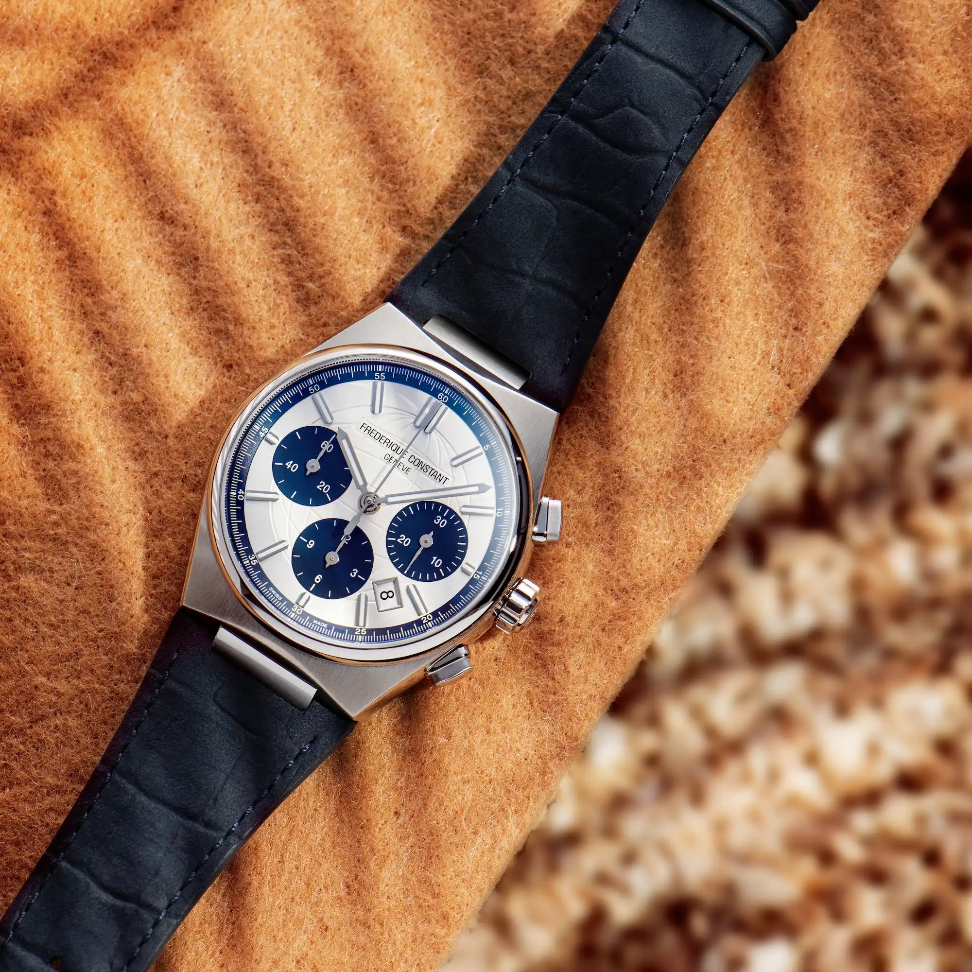 Produktfotografie des Automatic Chronographen mit blauen Akzenten und einem dunkelblauen Lederarmband von Frederique Constant aus der Highlife-Kollektion auf einem orangenen Hintergrund