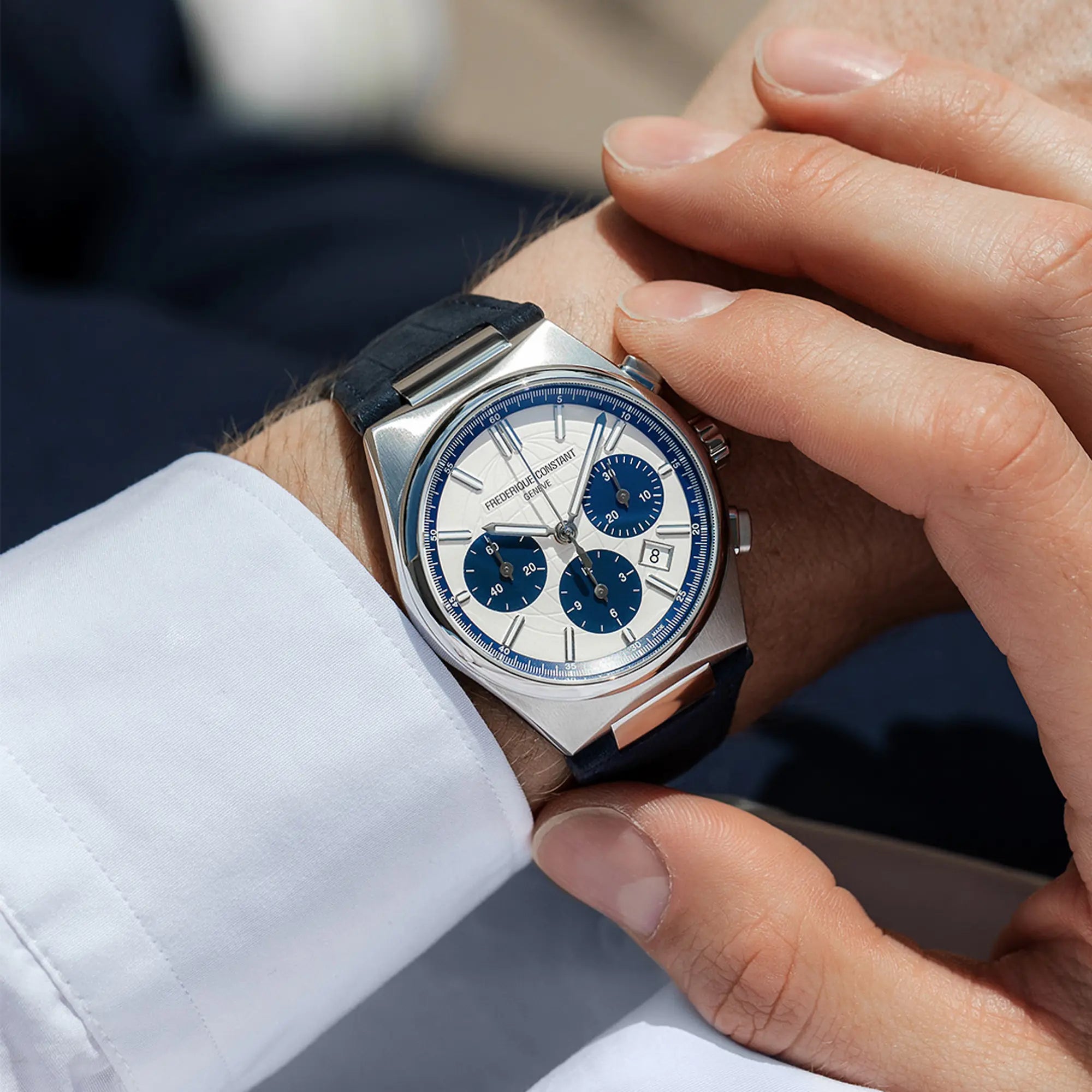 Mann trägt die Automatic Chronographen mit blauen Akzenten und einem dunkelblauen Lederarmband von Frederique Constant aus der Highlife-Kollektion auf einem orangenen Hintergrund an seinem Handgelenk und betätigt einen Pusher