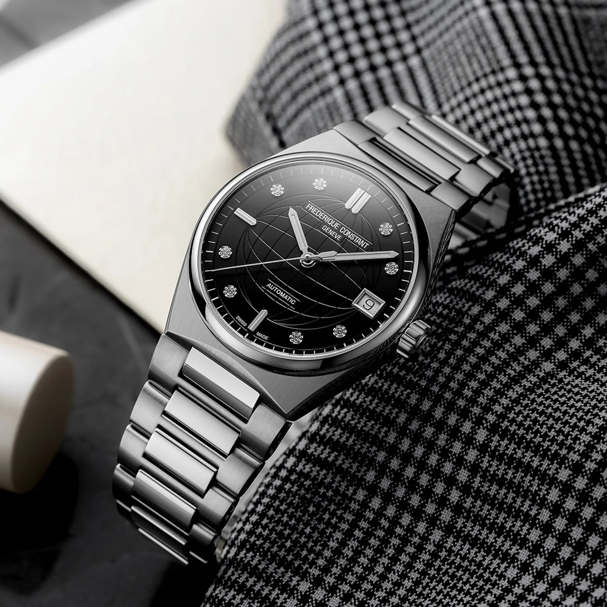 Produktfotografie der Frederique Constant Uhr "Highlife Ladies Automatic" mit einem schwarzen Zifferblatt mit Diamant-Indizes und Edelstahl-Gehäuse auf einem schwarz-weiß karierten Stofftuch