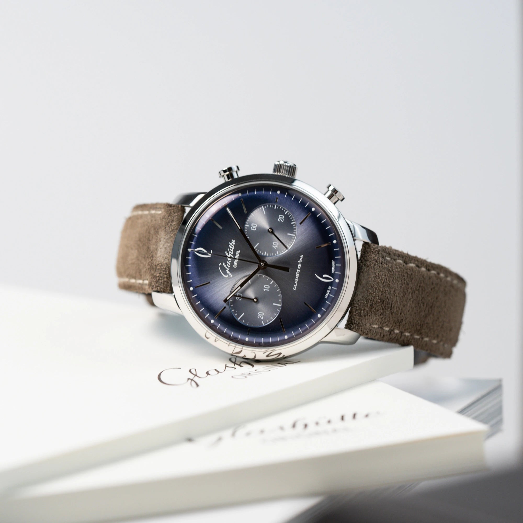 Produktfotografie der Glashütte Original Sixties Chronograph mit blauem Sonnenschliff-Zifferblatt, welche seitlich auf einem Glashütte Buch liegt