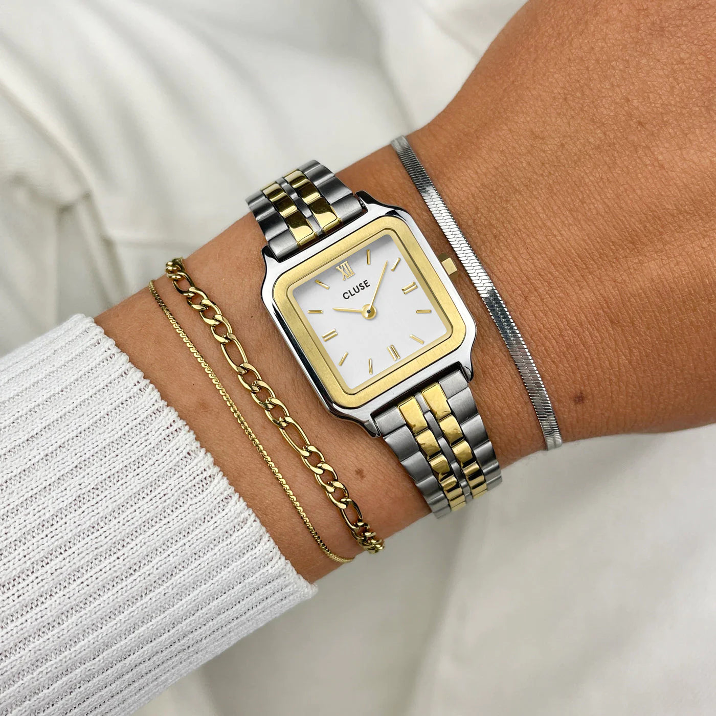 Frau trägt die Cluse Stahl-Uhr "Gracieuse Petite" in Stahl-Gold-Optik (bicolor) mit weißem Zifferblatt und kombiniert diese mit drei Armbändern