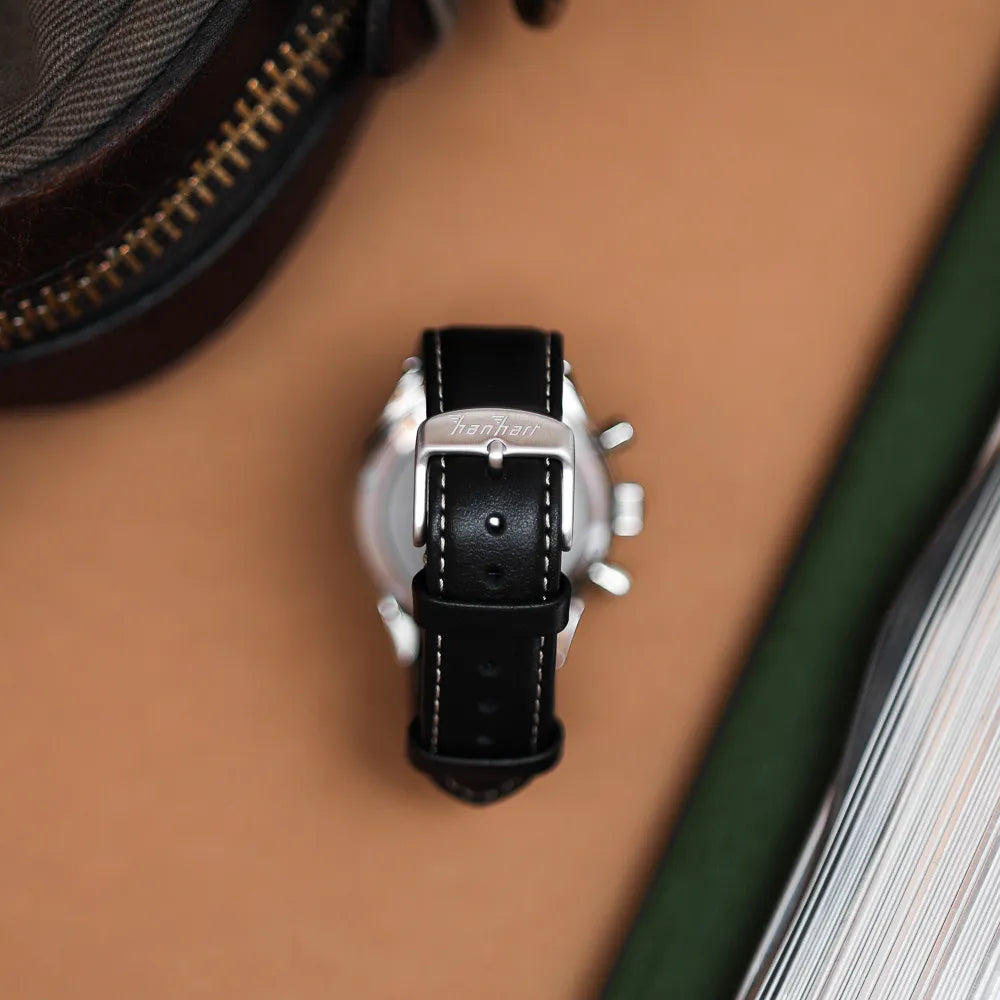 Produktfotografie des Hanhart 415 ES Pure Chronographen in Edelstahl mit weißen und roten Details am Lederband mit Blick auf die Edelstahl-Dornshcliesse