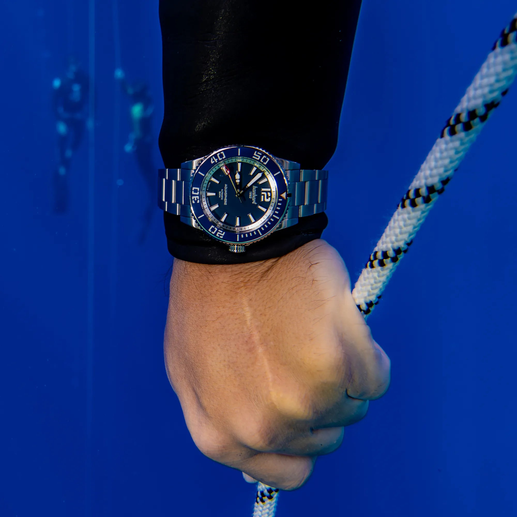 Mann taucht unter Wasser und hält sich an einem Seil fest, während er die Hanhart Aquasphere Uhr am Handgelenk trägt