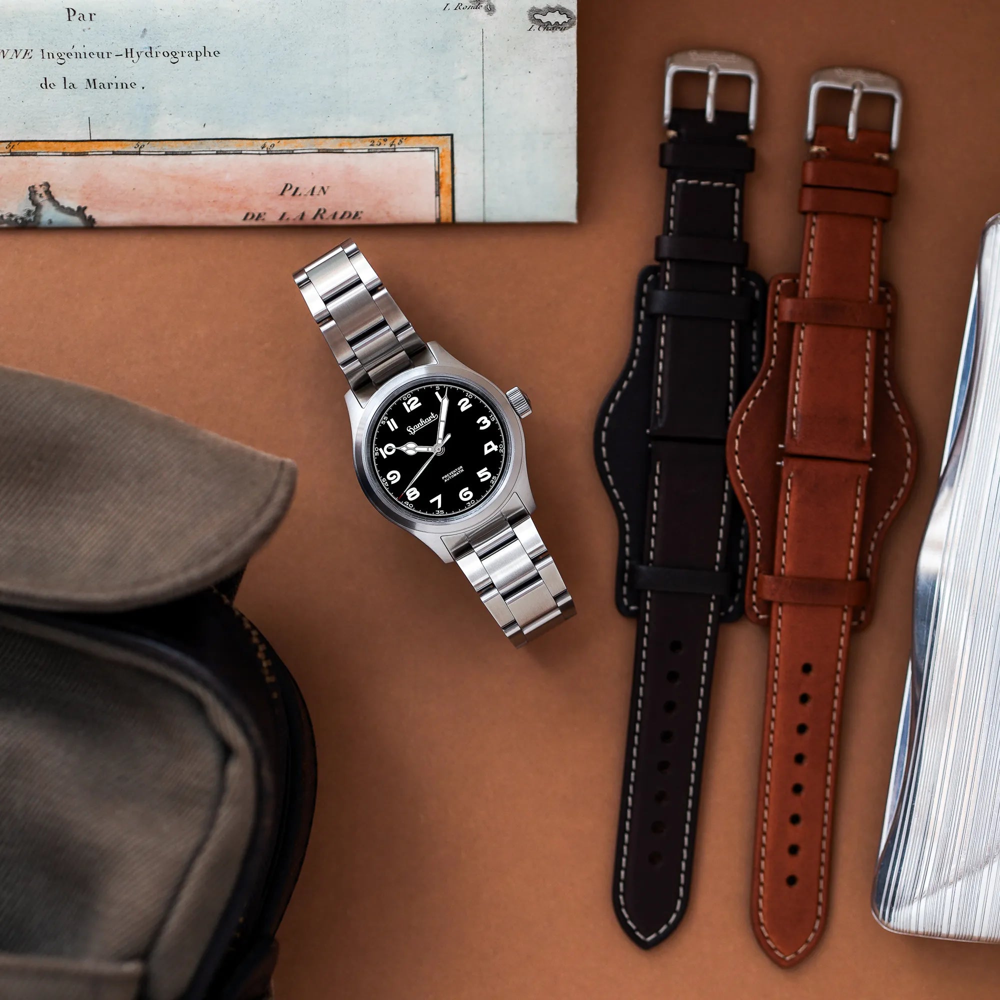Produktfotografie der Hanhart Preventor HD12 Dreizeiger-Uhr mit schwarzem Zifferblatt zusammen mit den verschiedenen alternativen Lederbändern in schwarz und braun