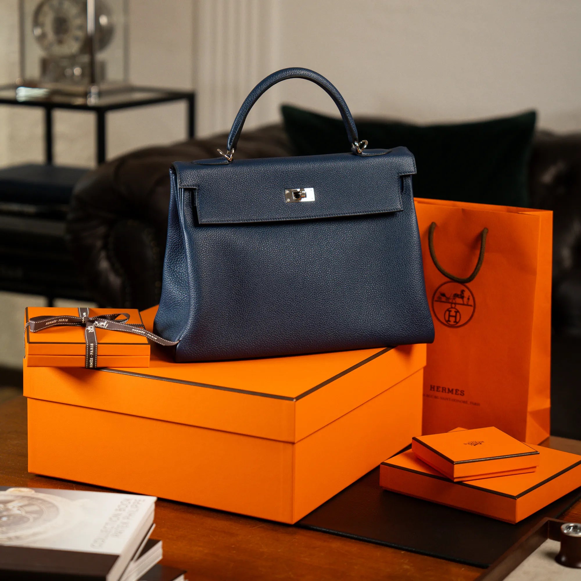 Produktfotografie der Hermes Kelly Bag 32 aus Togo-Kalbsleder in der Farbe Bleu-de-Prusse mit silberner Hardware, während die Tasche auf dem orangenem Hermes Karton
