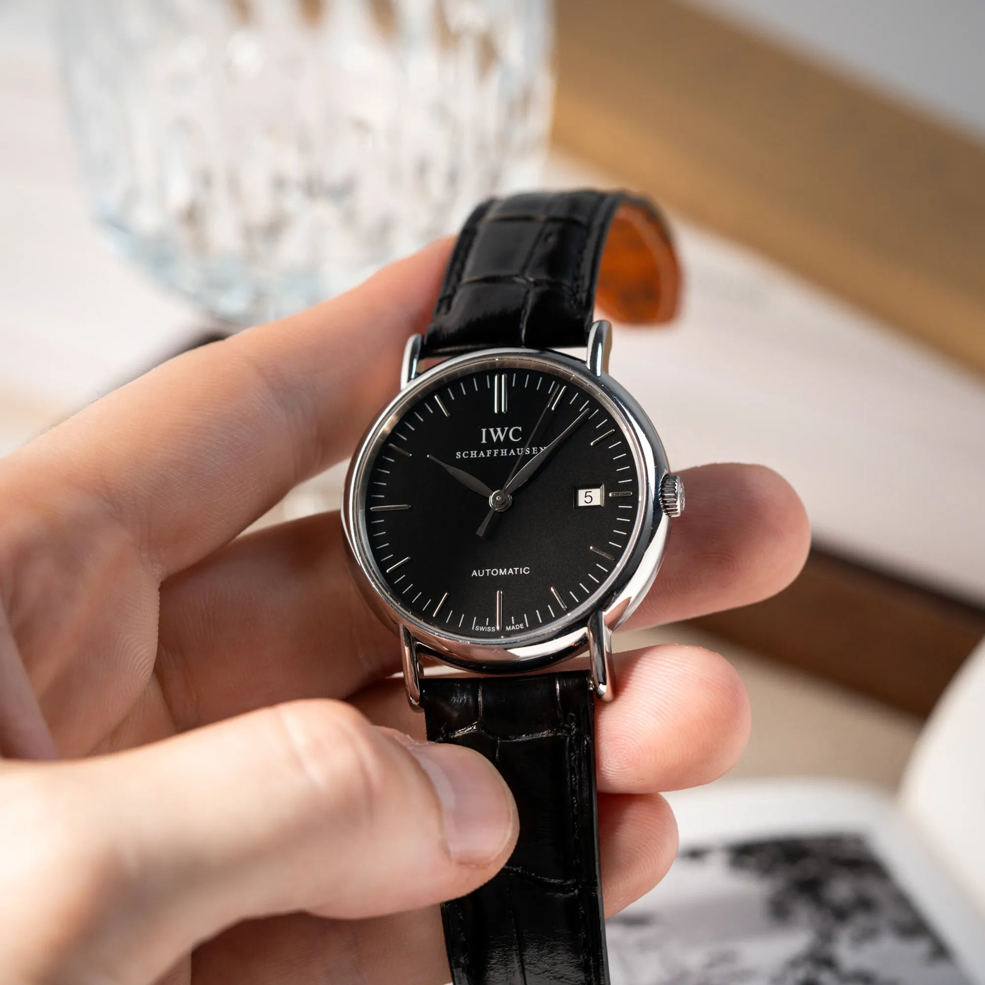 Mann hält die IWC Portofino Automatik IW356305 Armbanduhr mit minimalistischen, schwarzem Zifferblatt mit Stichindizes am schwarzen Lederband in seiner Hand
