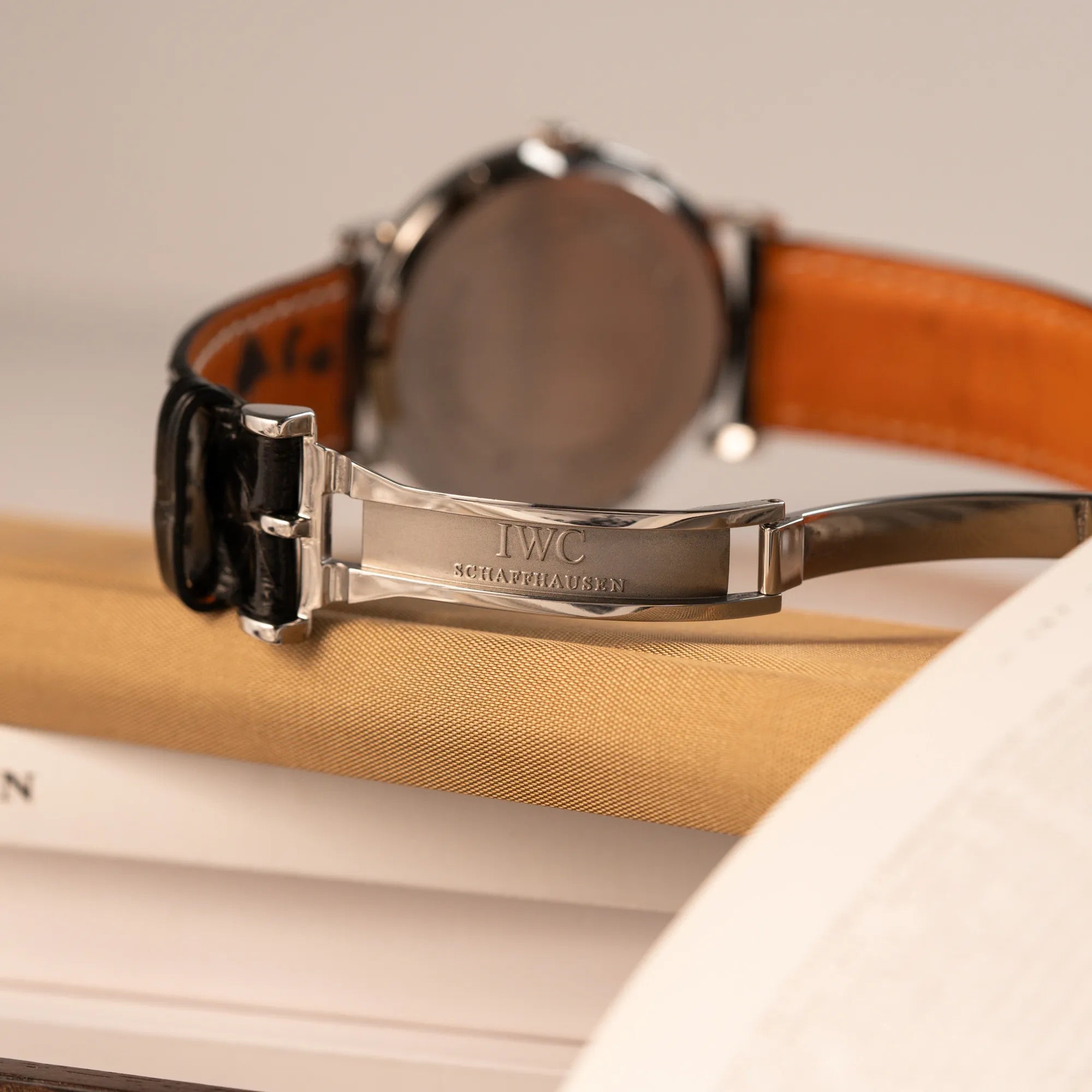 Produktfotografie zeigt das IWC Logo der IWC Portofino Automatik IW356305 Armbanduhr mit minimalistischen, schwarzem Zifferblatt mit Stichindizes am schwarzen Lederband