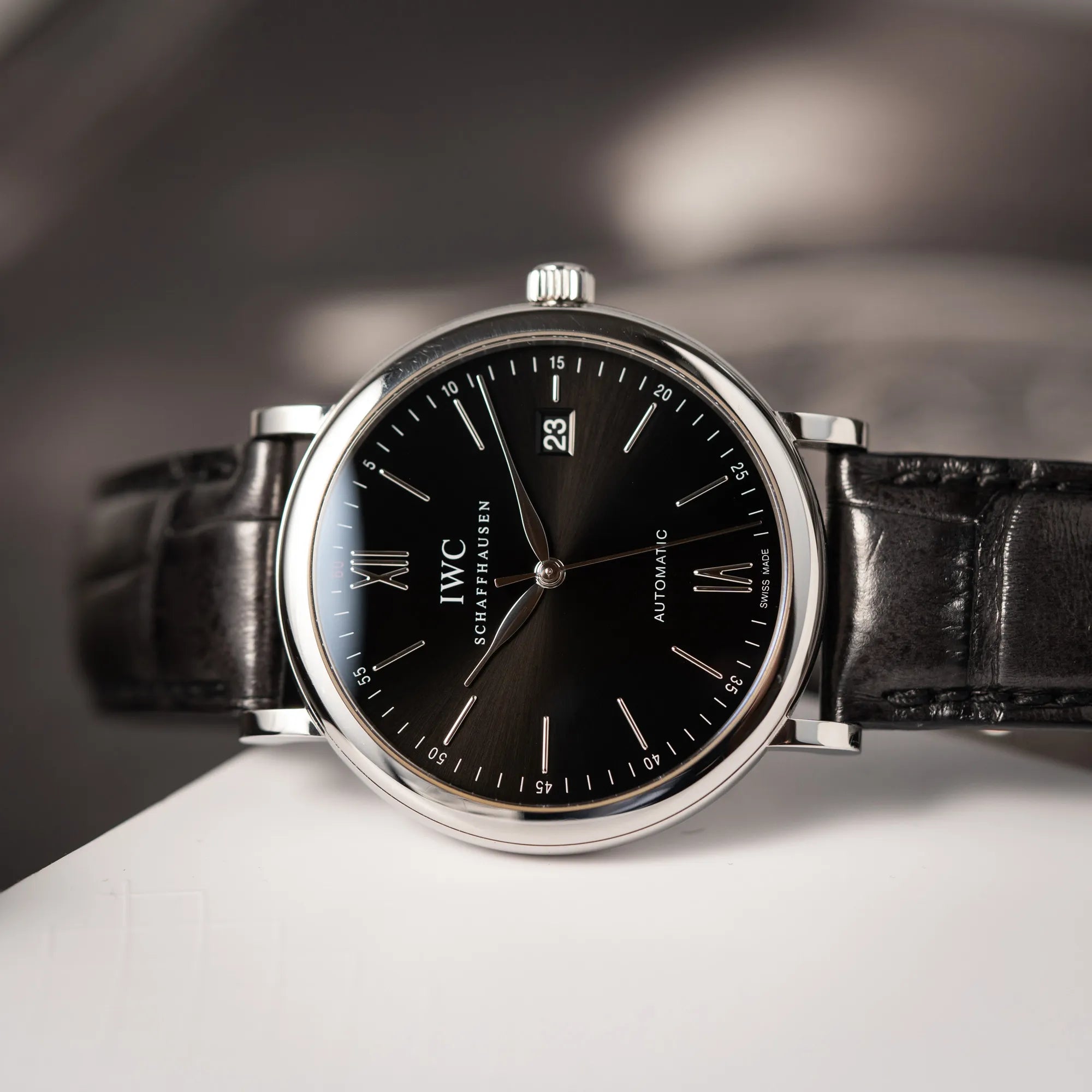 IWC Portofino 40 Automatik Armbanduhr mit schwarzem Zifferblatt am schwarzen Lederband liegt seitlich auf dem Uhrengehäuse