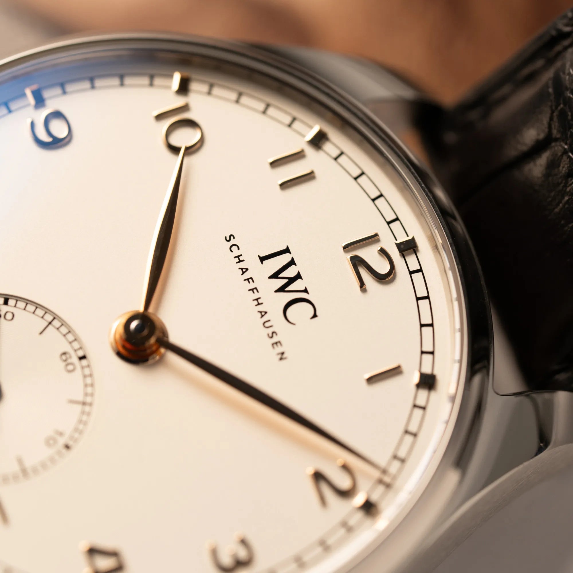 Detailaufnahme der IWC Portugieser 40 Automatik IW358303 mit weißem Zifferblatt und roségoldenen Zeiger- und Index-Details am schwarzen Lederband
