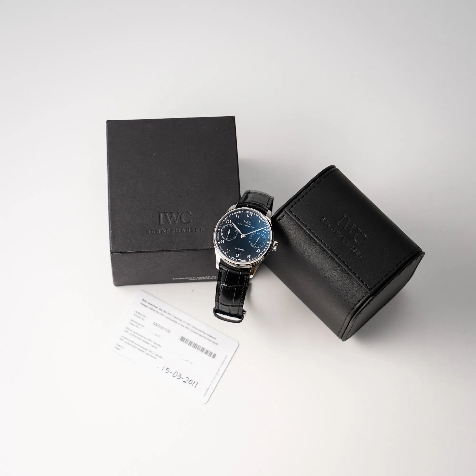 IWC Portugieser 7 Days IW500109 mit schwarzem Zifferblatt am schwarzen Lederband zusammen mit dem Lieferumfang, betsehend aus IWC Travel Box und Garantiekarte